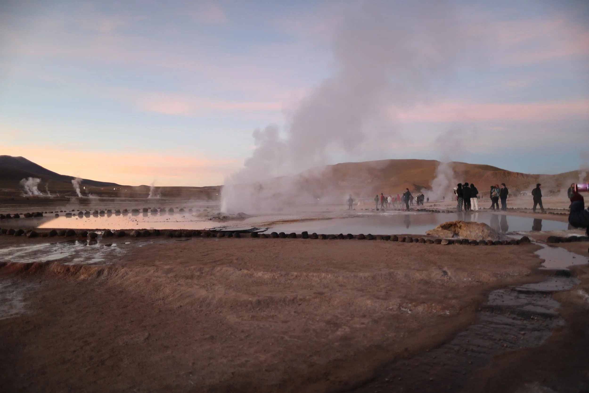 Steam rising from the El Tatio Geysers at sunrise, surrounded by the dramatic volcanic landscape of the Atacama Desert in northern Chile.