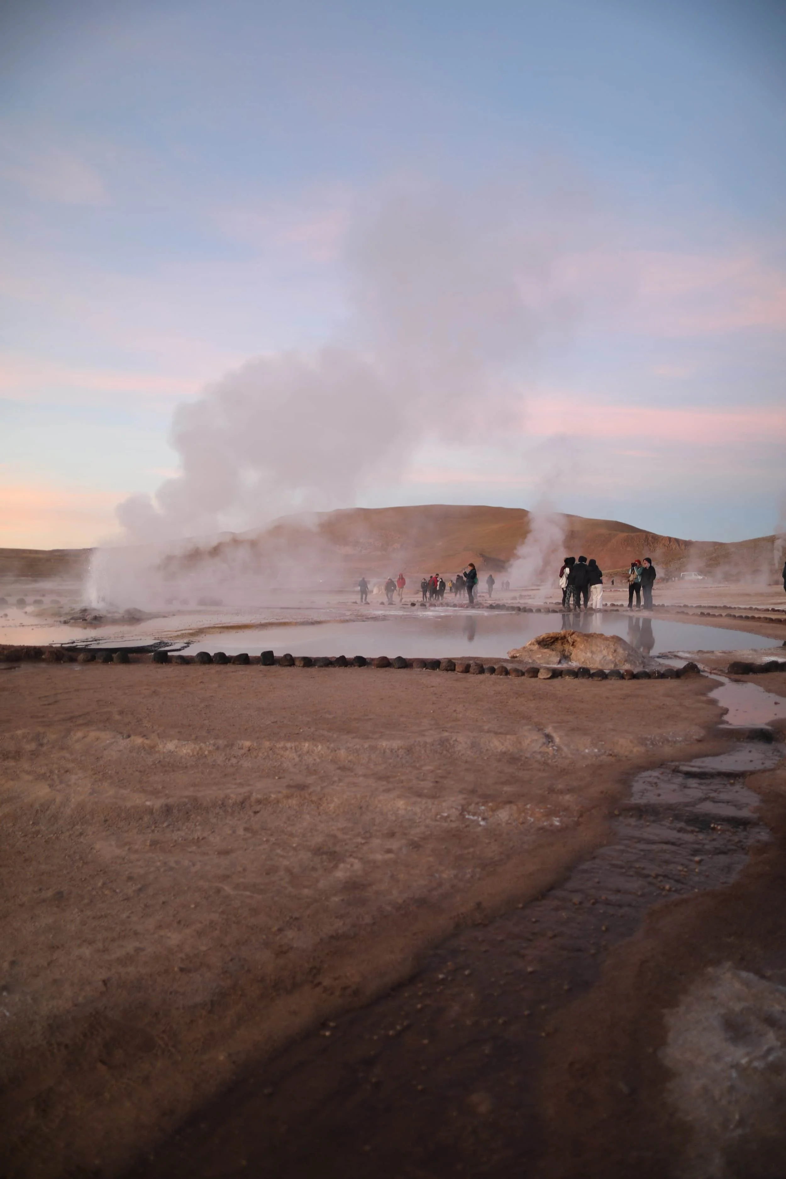 Steam rising from the El Tatio Geysers at sunrise, surrounded by the dramatic volcanic landscape of the Atacama Desert in northern Chile.