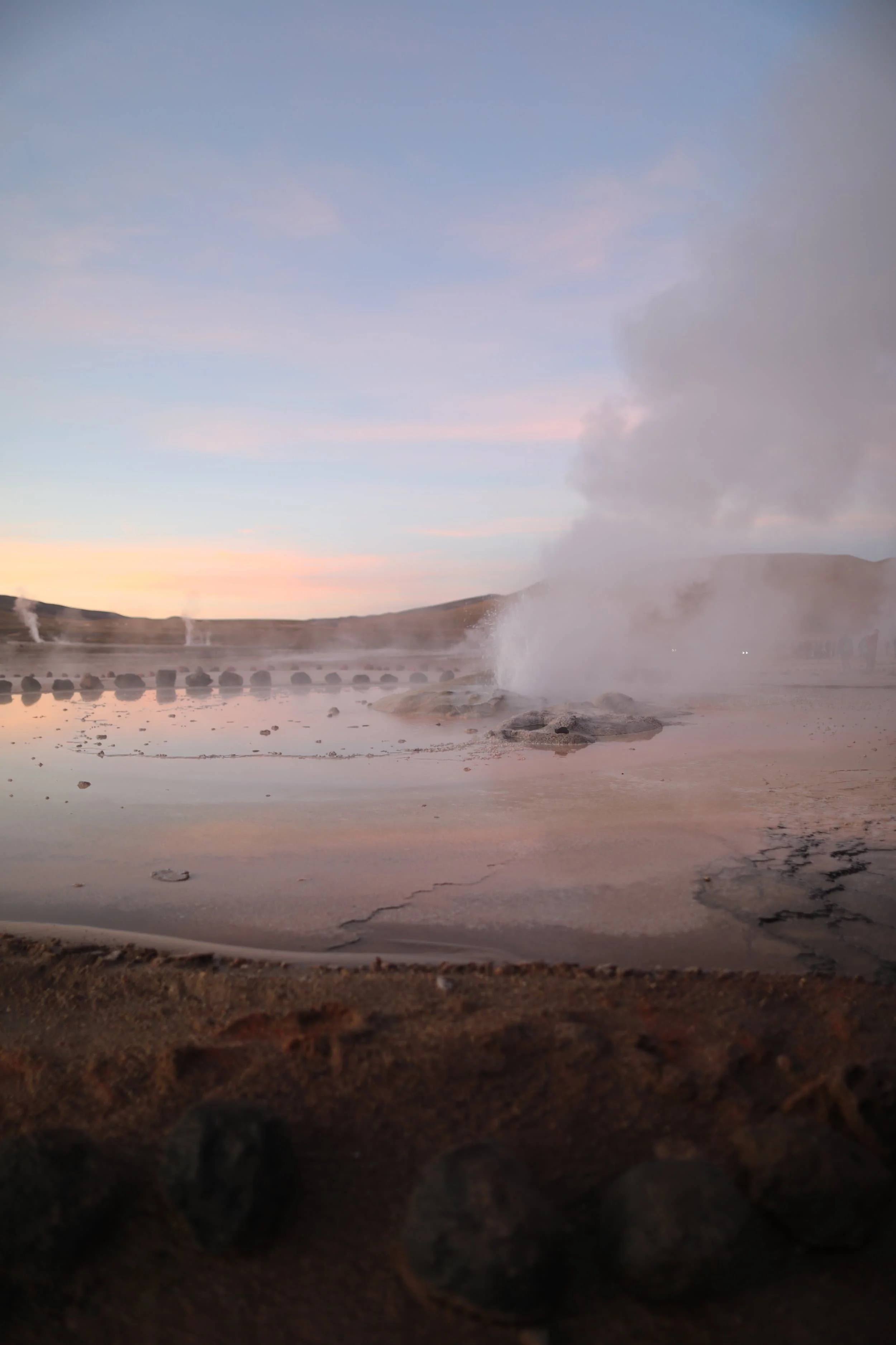 Steam rising from the El Tatio Geysers at sunrise, surrounded by the dramatic volcanic landscape of the Atacama Desert in northern Chile.