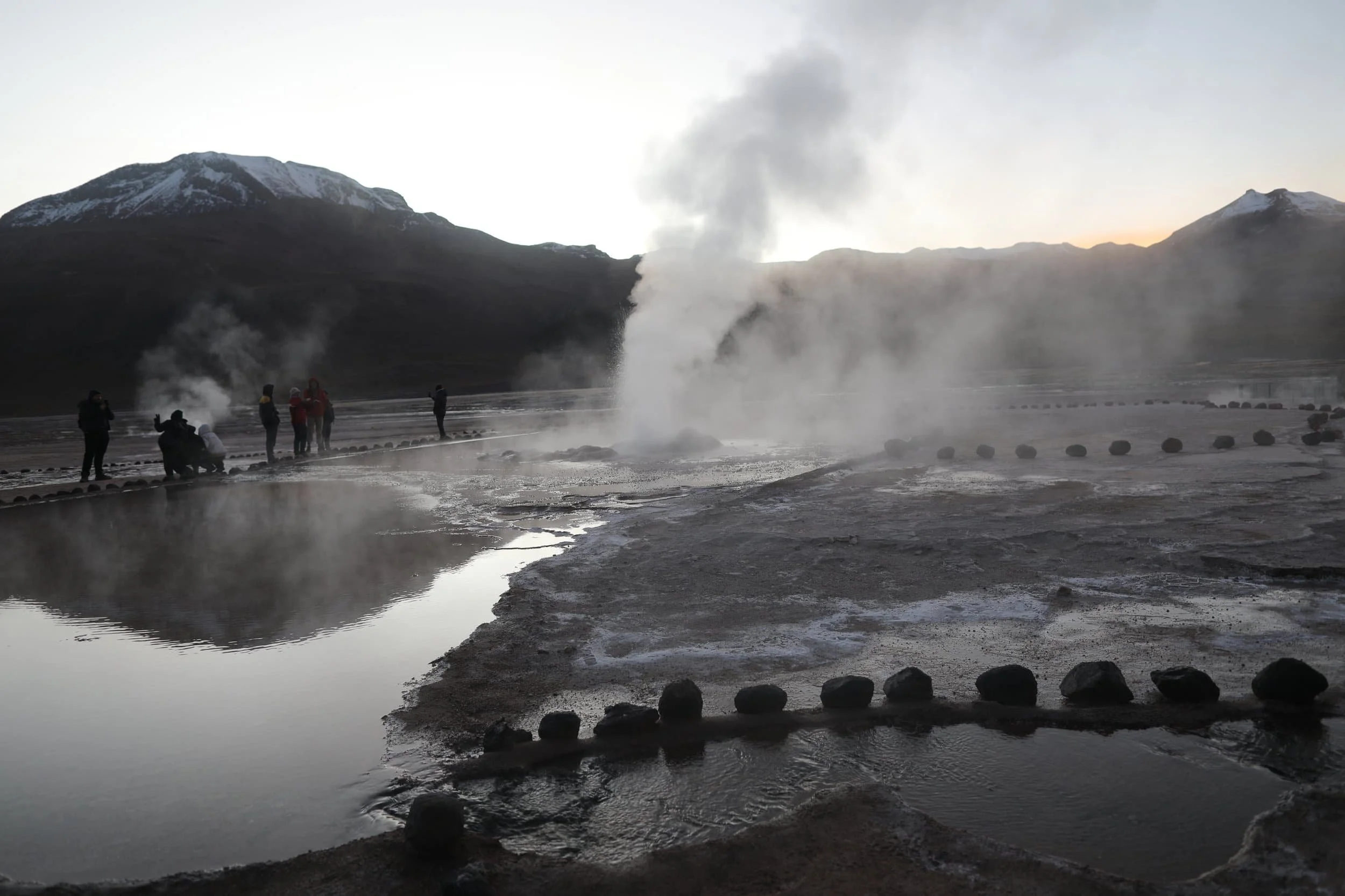 Steam rising from the El Tatio Geysers at sunrise, surrounded by the dramatic volcanic landscape of the Atacama Desert in northern Chile.