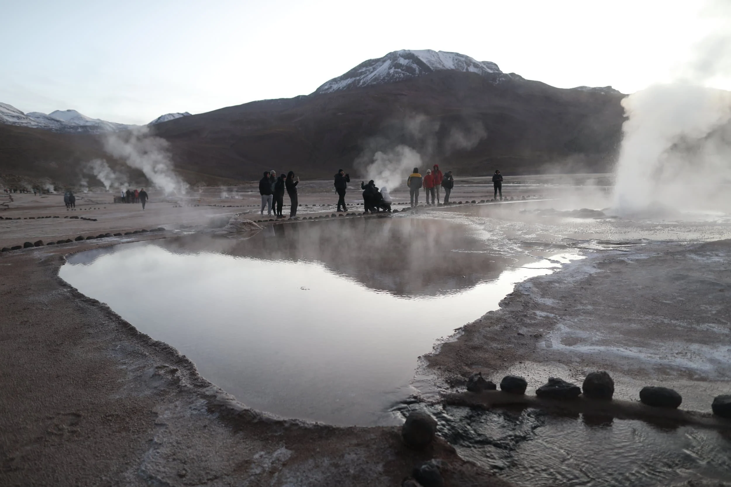 Steam rising from the El Tatio Geysers at sunrise, surrounded by the dramatic volcanic landscape of the Atacama Desert in northern Chile.