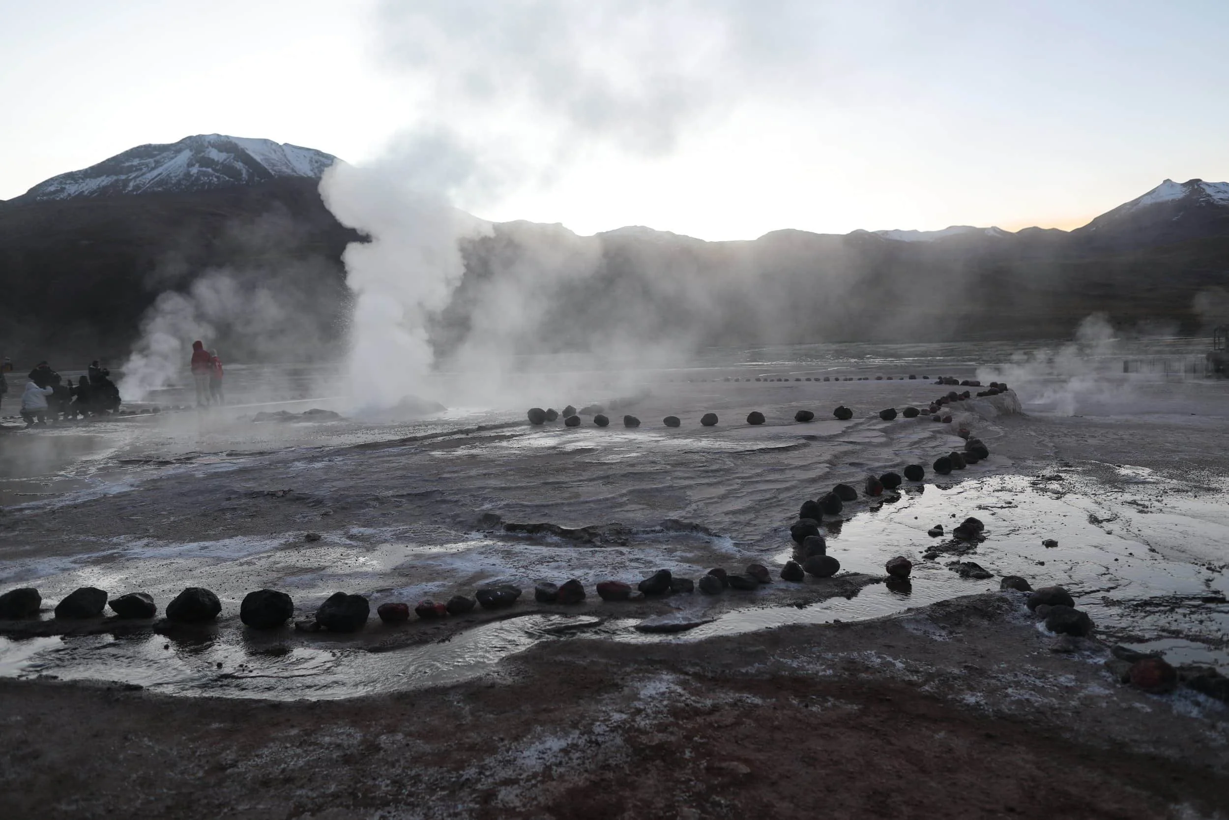 Steam rising from the El Tatio Geysers at sunrise, surrounded by the dramatic volcanic landscape of the Atacama Desert in northern Chile.