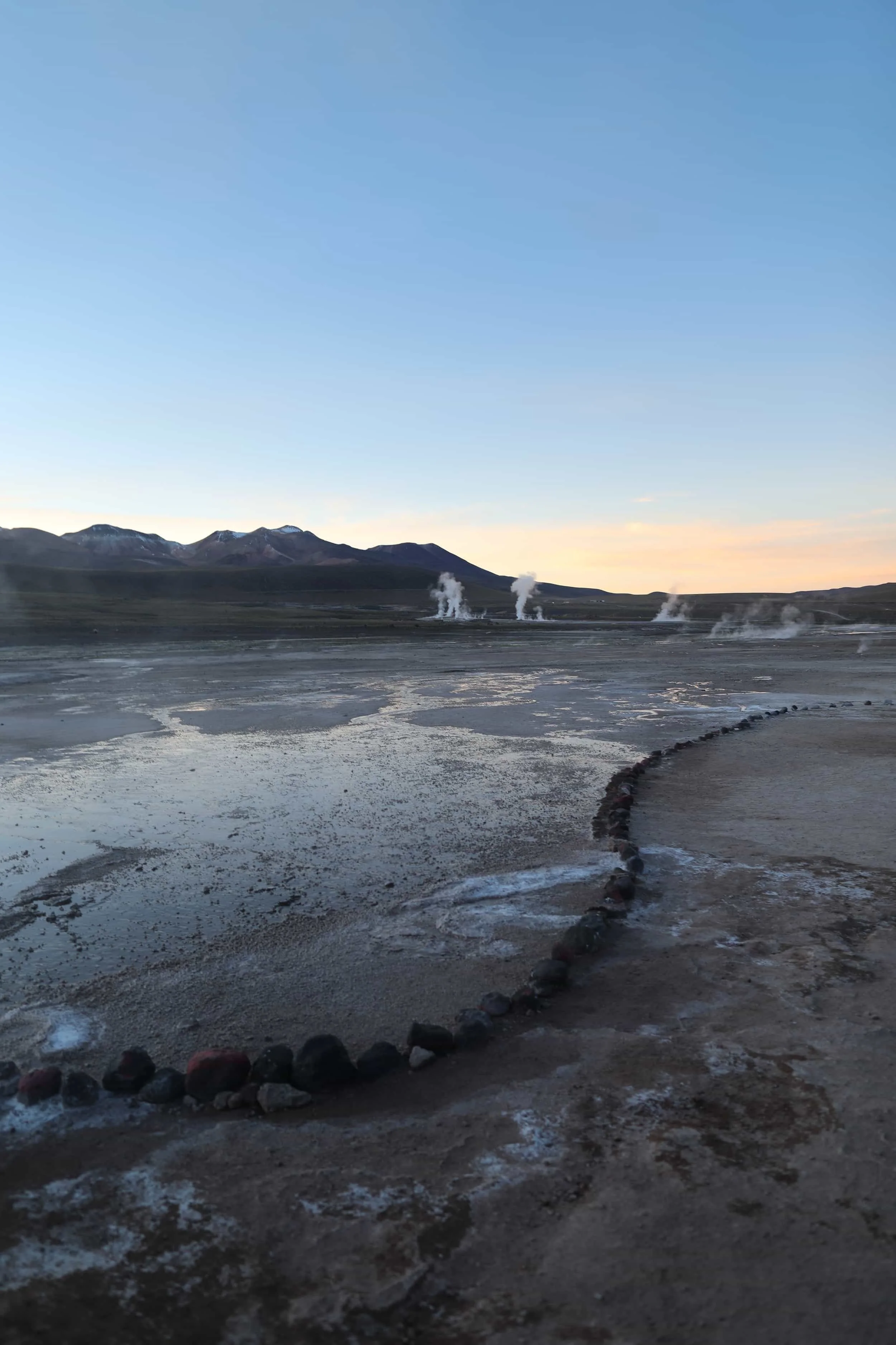 Steam rising from the El Tatio Geysers at sunrise, surrounded by the dramatic volcanic landscape of the Atacama Desert in northern Chile.
