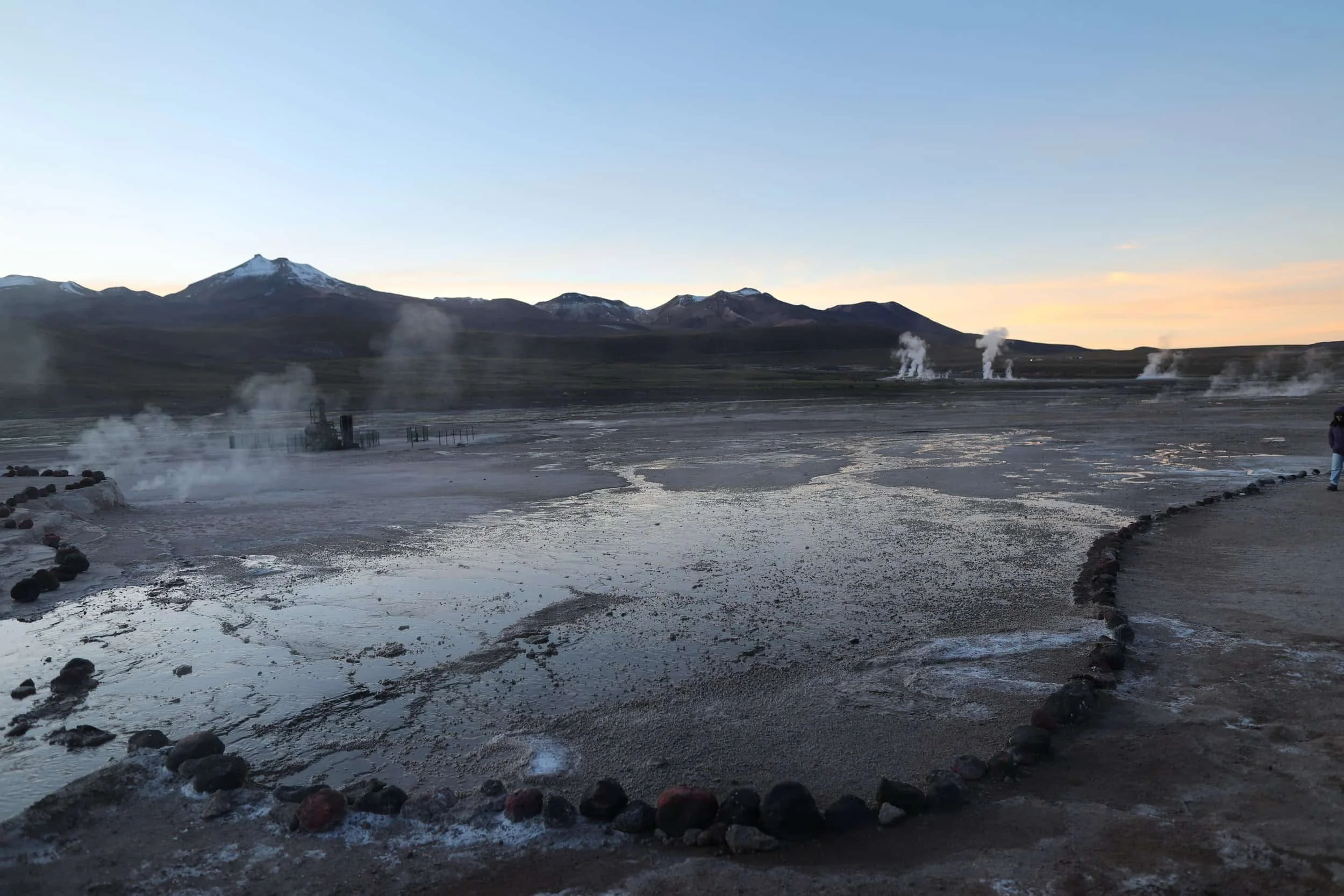 Steam rising from the El Tatio Geysers at sunrise, surrounded by the dramatic volcanic landscape of the Atacama Desert in northern Chile.