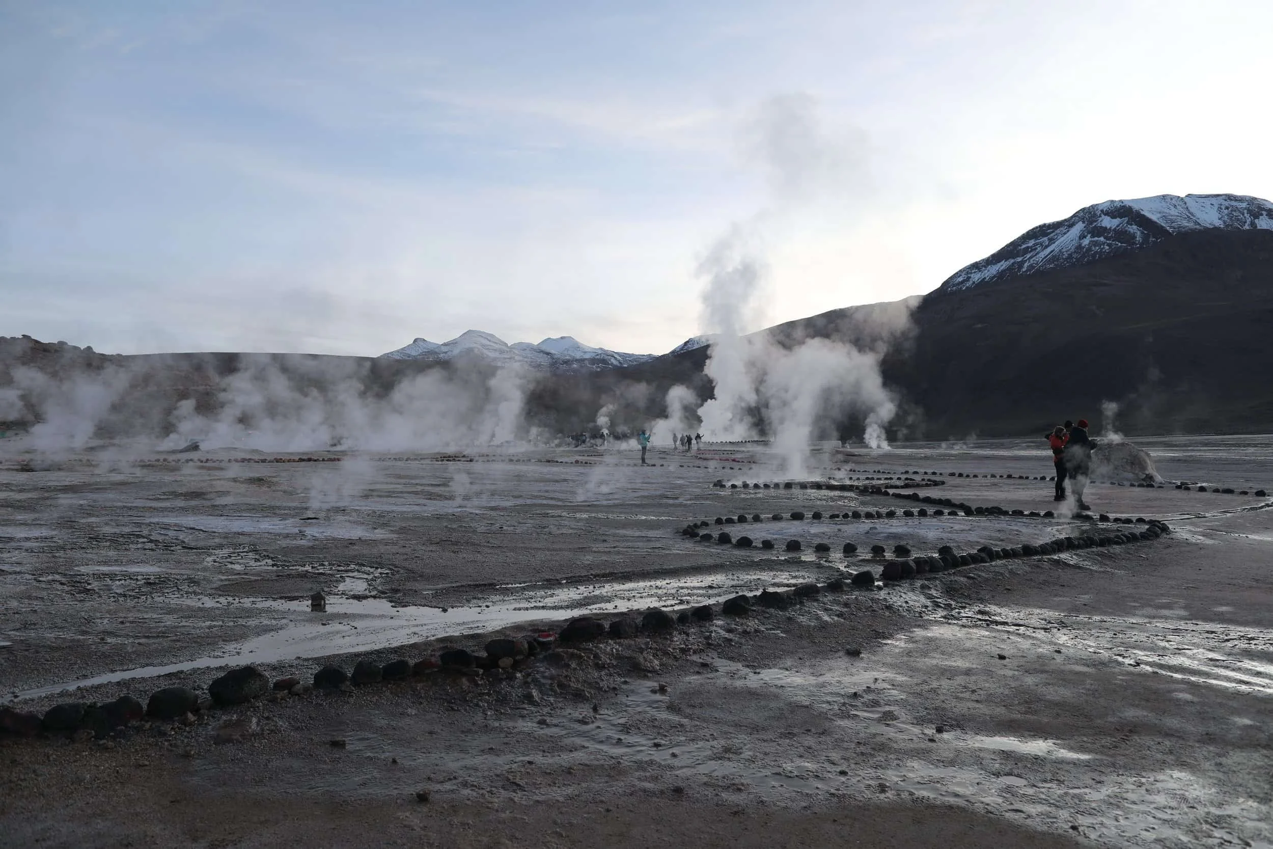Steam rising from the El Tatio Geysers at sunrise, surrounded by the dramatic volcanic landscape of the Atacama Desert in northern Chile.