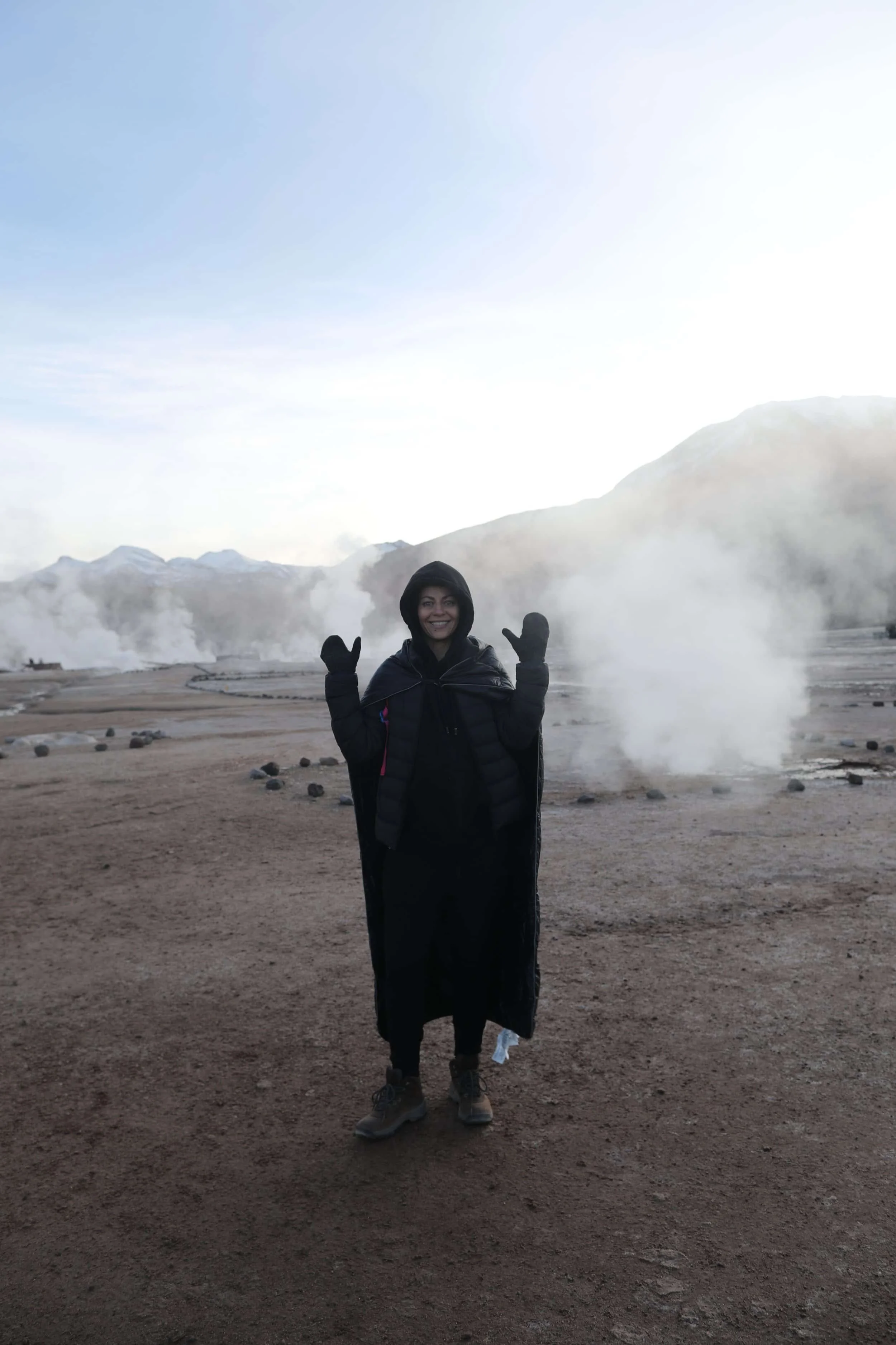  Girl with steam rising from the El Tatio Geysers at sunrise, surrounded by the dramatic volcanic landscape of the Atacama Desert in northern Chile. 