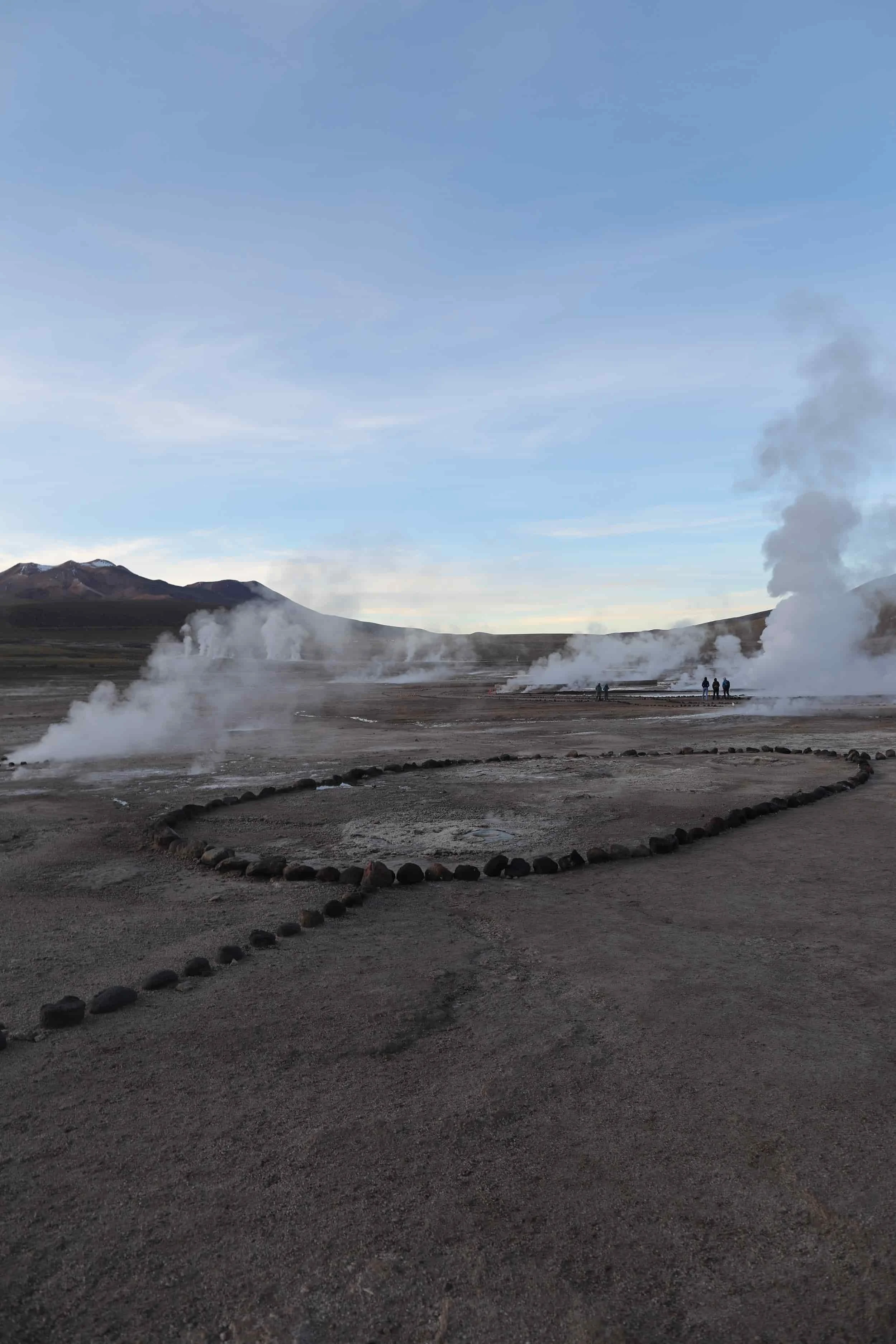 Steam rising from the El Tatio Geysers at sunrise, surrounded by the dramatic volcanic landscape of the Atacama Desert in northern Chile.