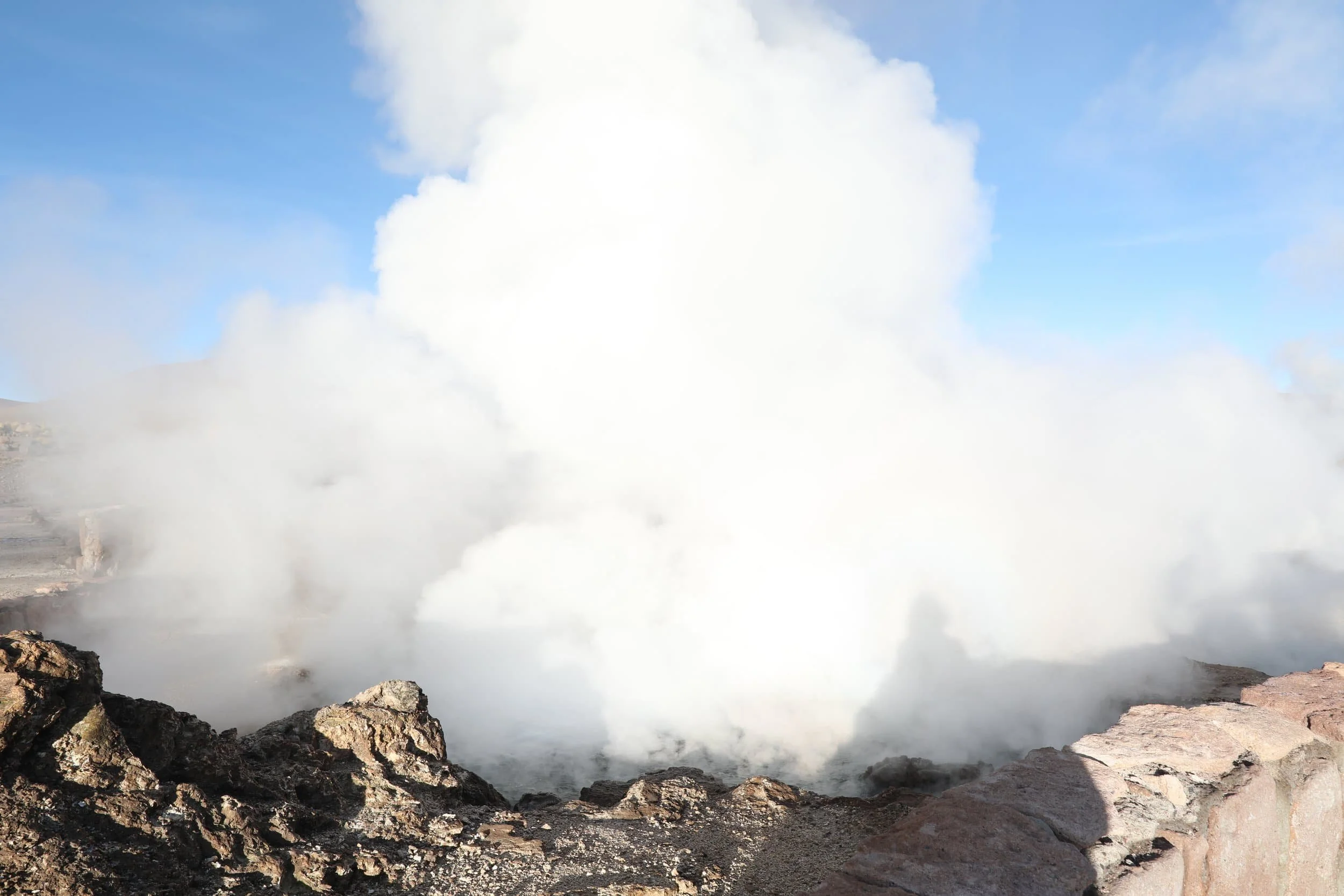 Powerful steam rising from the Assassin Geyser, surrounded by dark mineral formations at El Tatio in Chile.