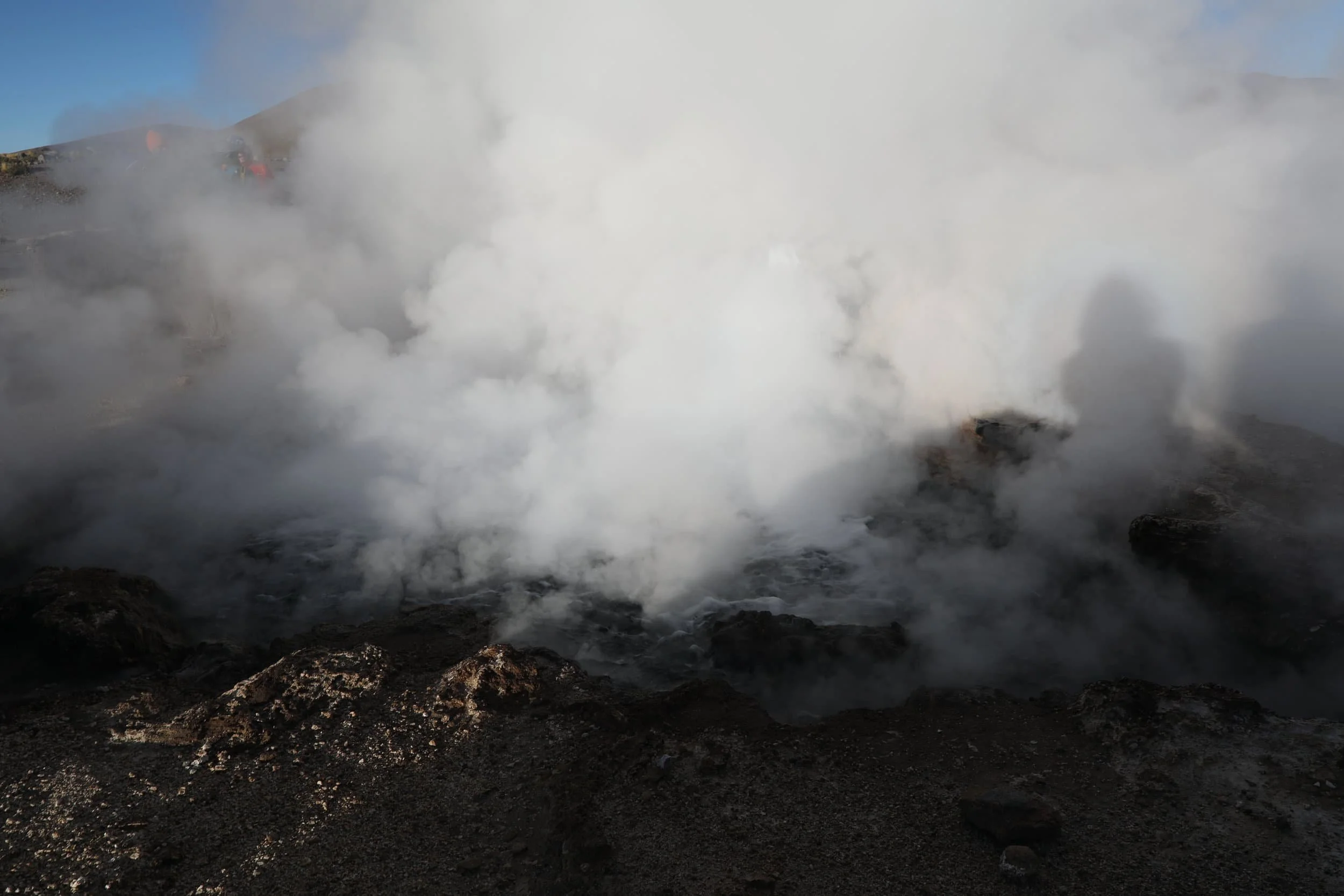 Powerful steam rising from the Assassin Geyser, surrounded by dark mineral formations at El Tatio in Chile.