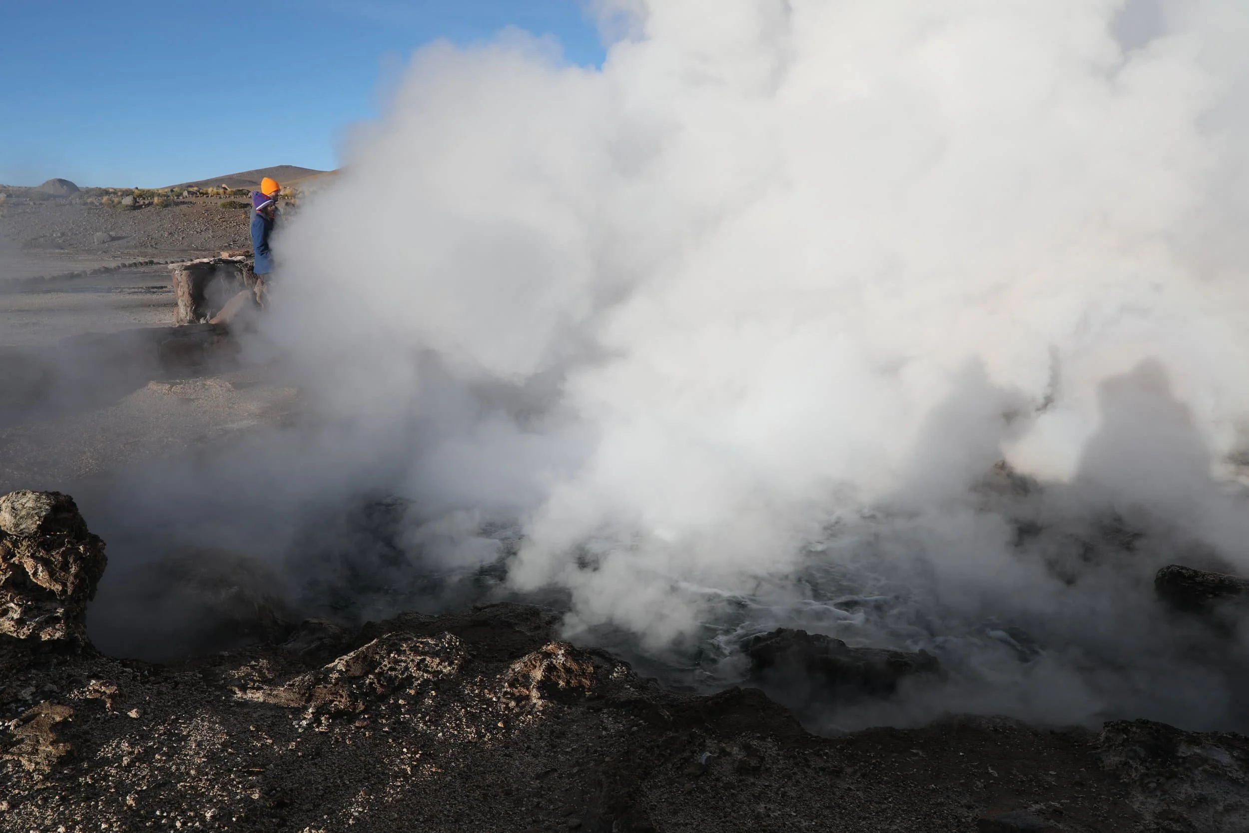 Powerful steam rising from the Assassin Geyser, surrounded by dark mineral formations at El Tatio in Chile.