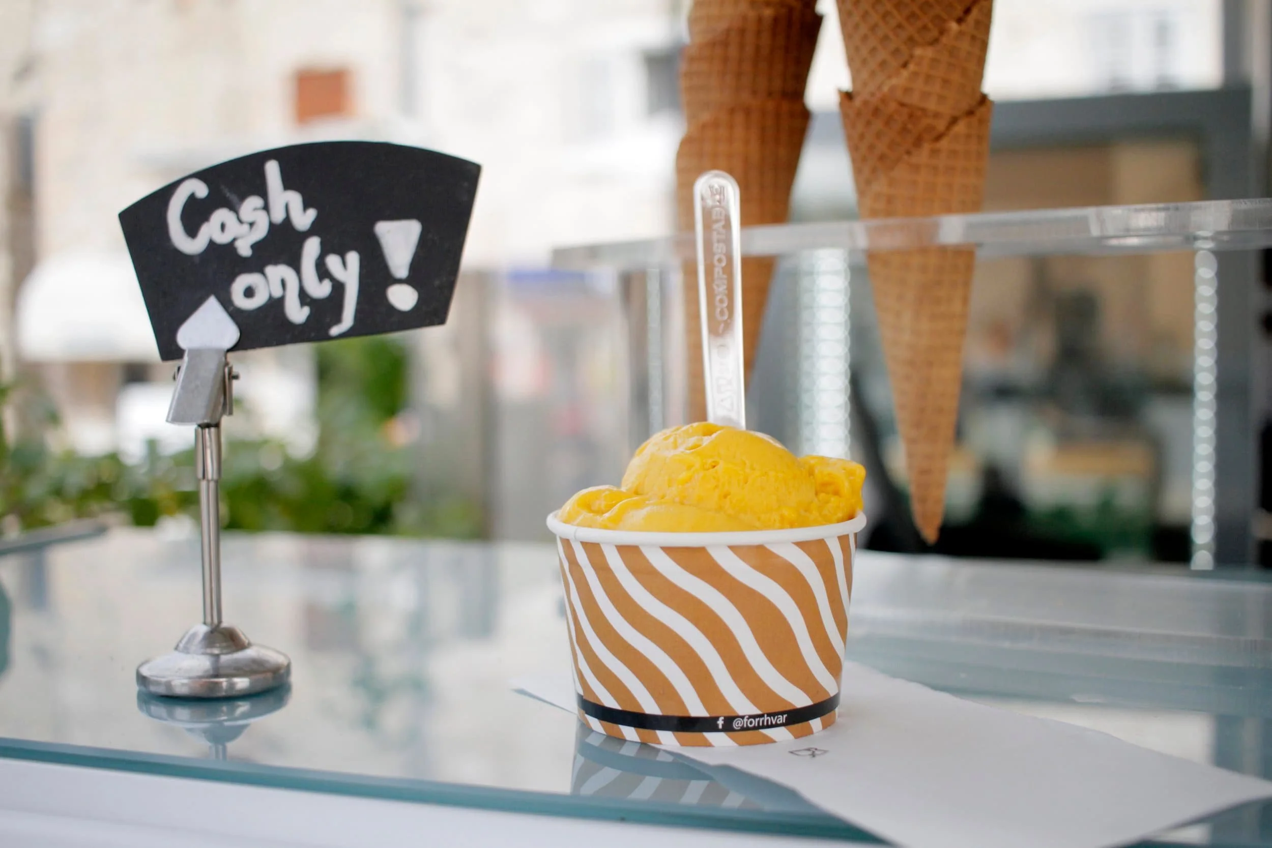 Mango ice cream in a cup on a counter with a spoon and sign nearby