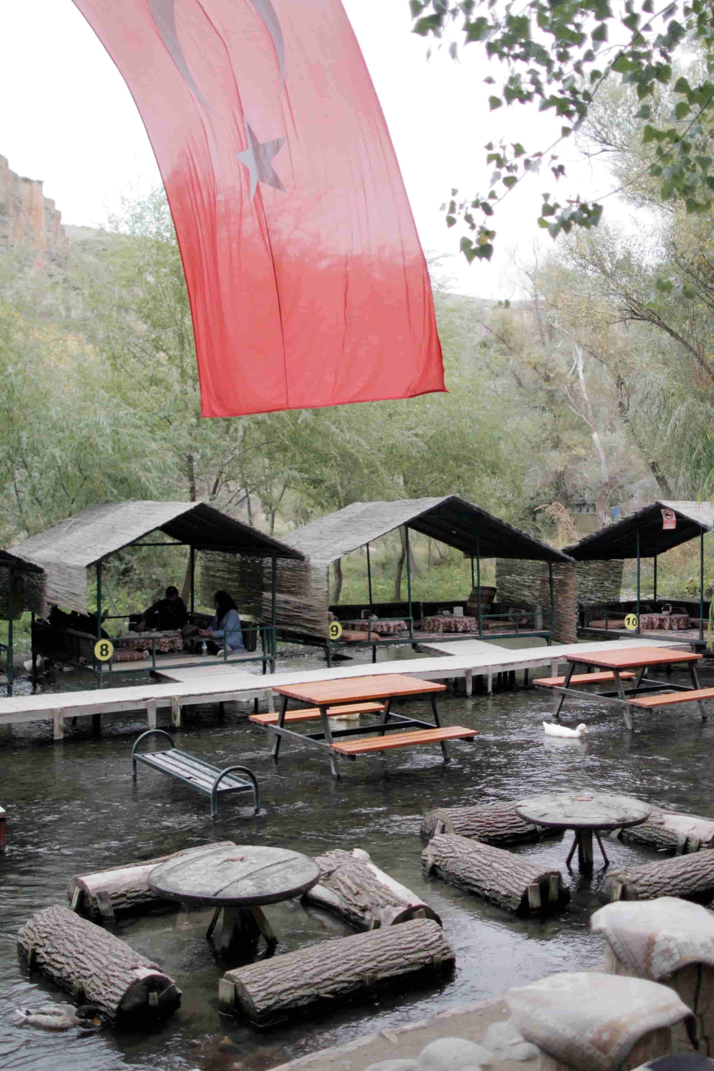 Red Turkish flag waving above outdoor eating area along the river with tables at Ihlara Valley in Cappadocia Turkey