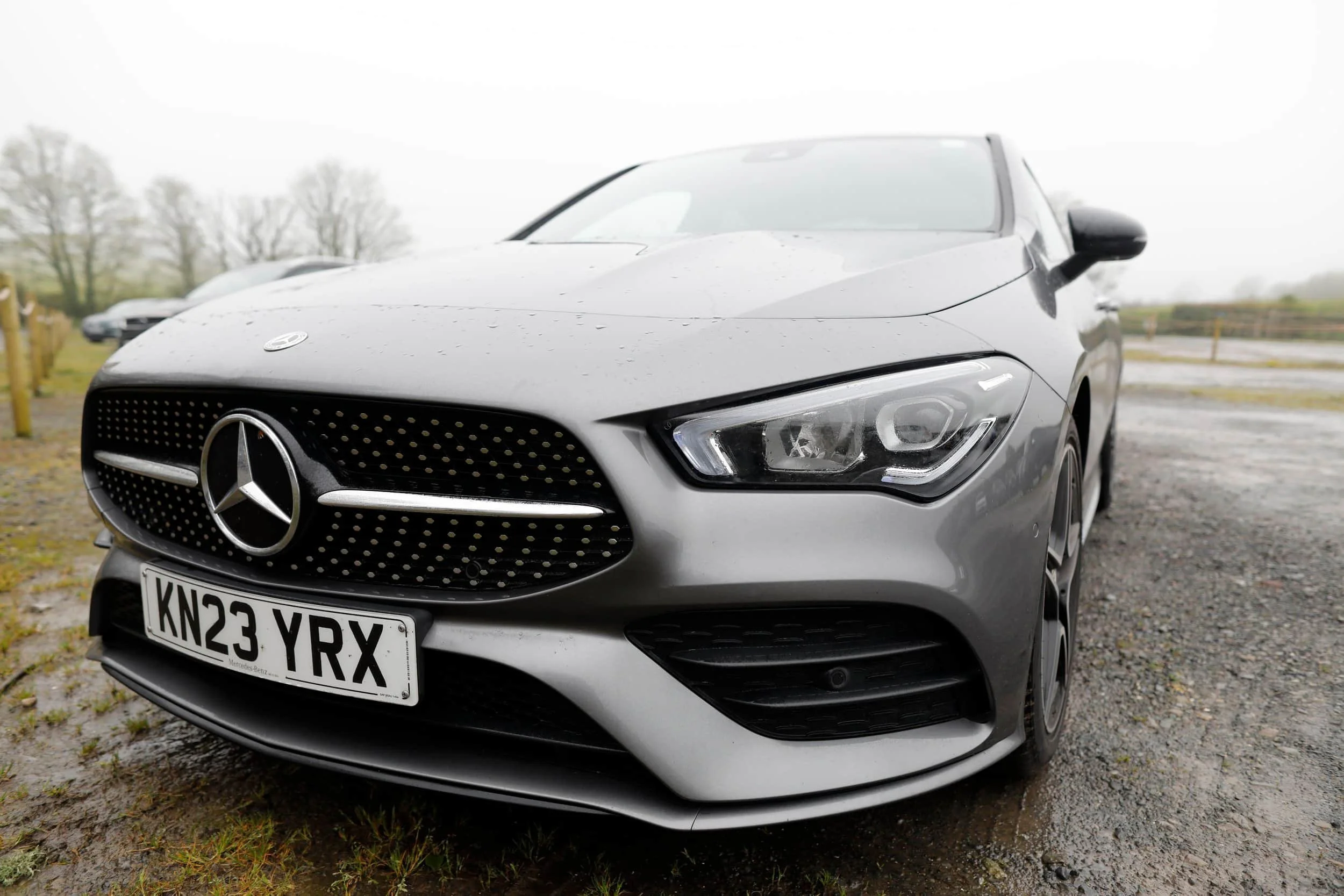Close up of front of grey Mercedes vehicle with wet ground and landscape beyond