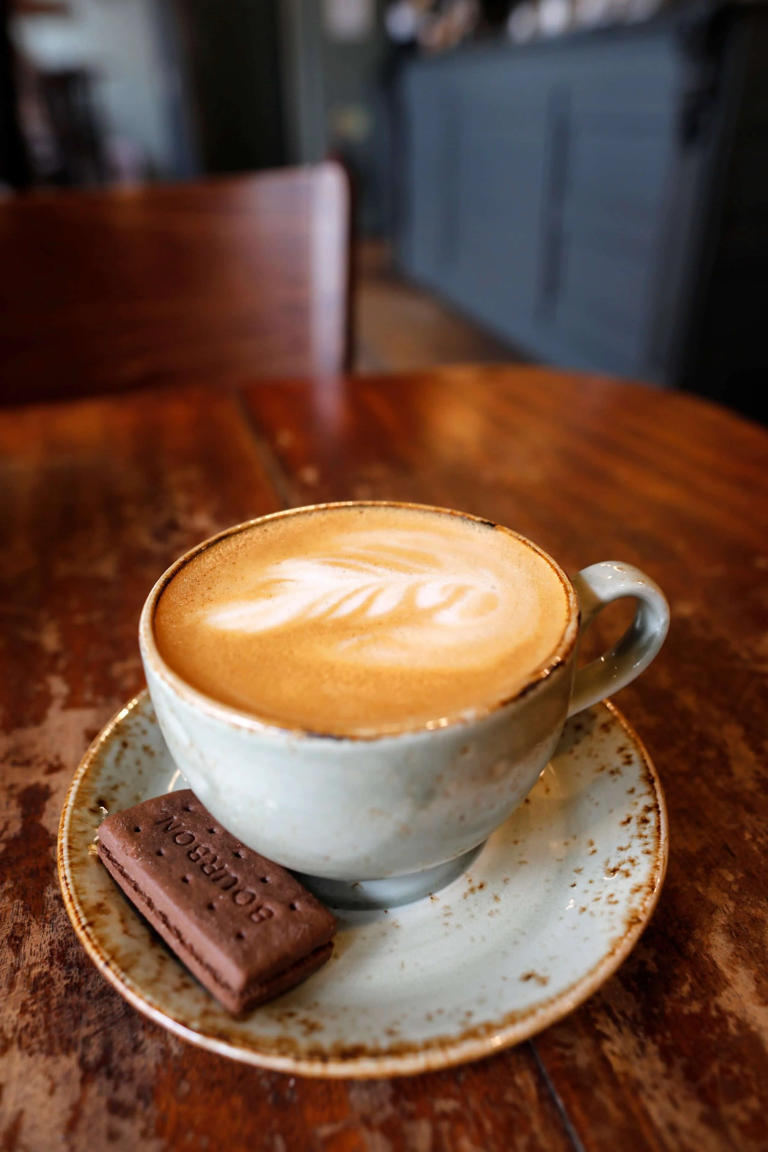 Cup of coffee in a ceramic cup with a small chocolate biscuit on the small plate on a wooden table
