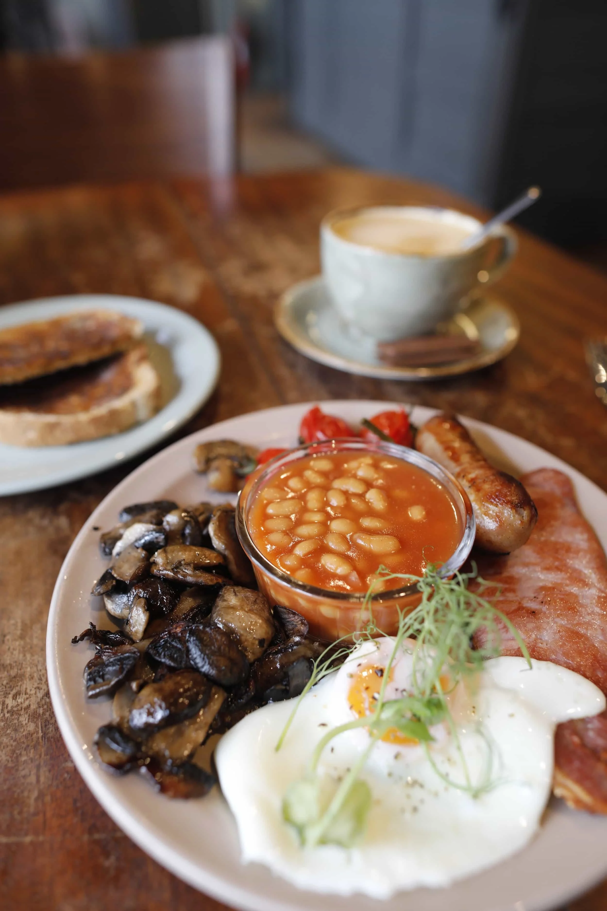 Full English breakfast plate on a wooden table with beans, mushrooms, eggs, tomatoes and bacon