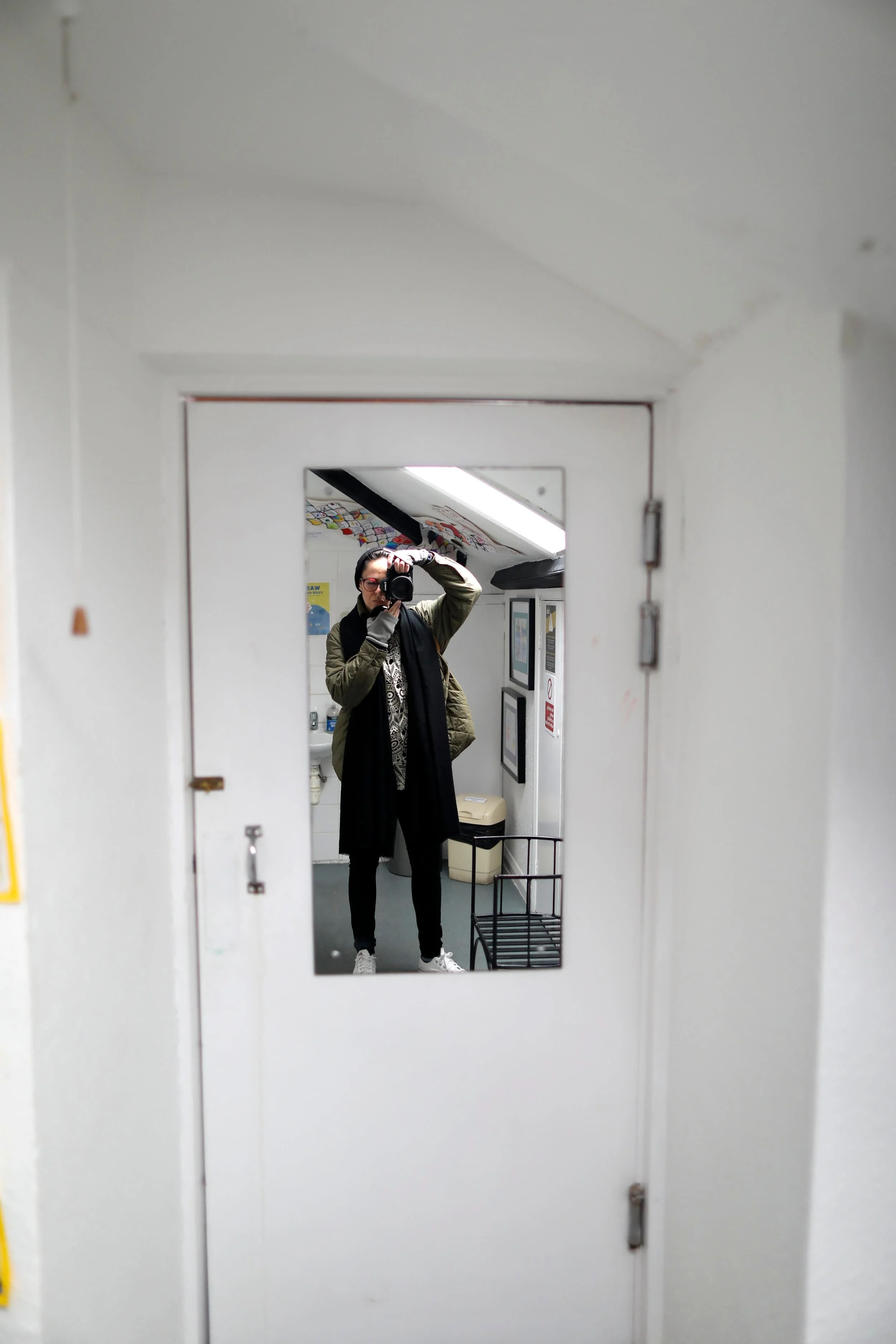 A girl wearing black taking photo of herself in a white bathroom