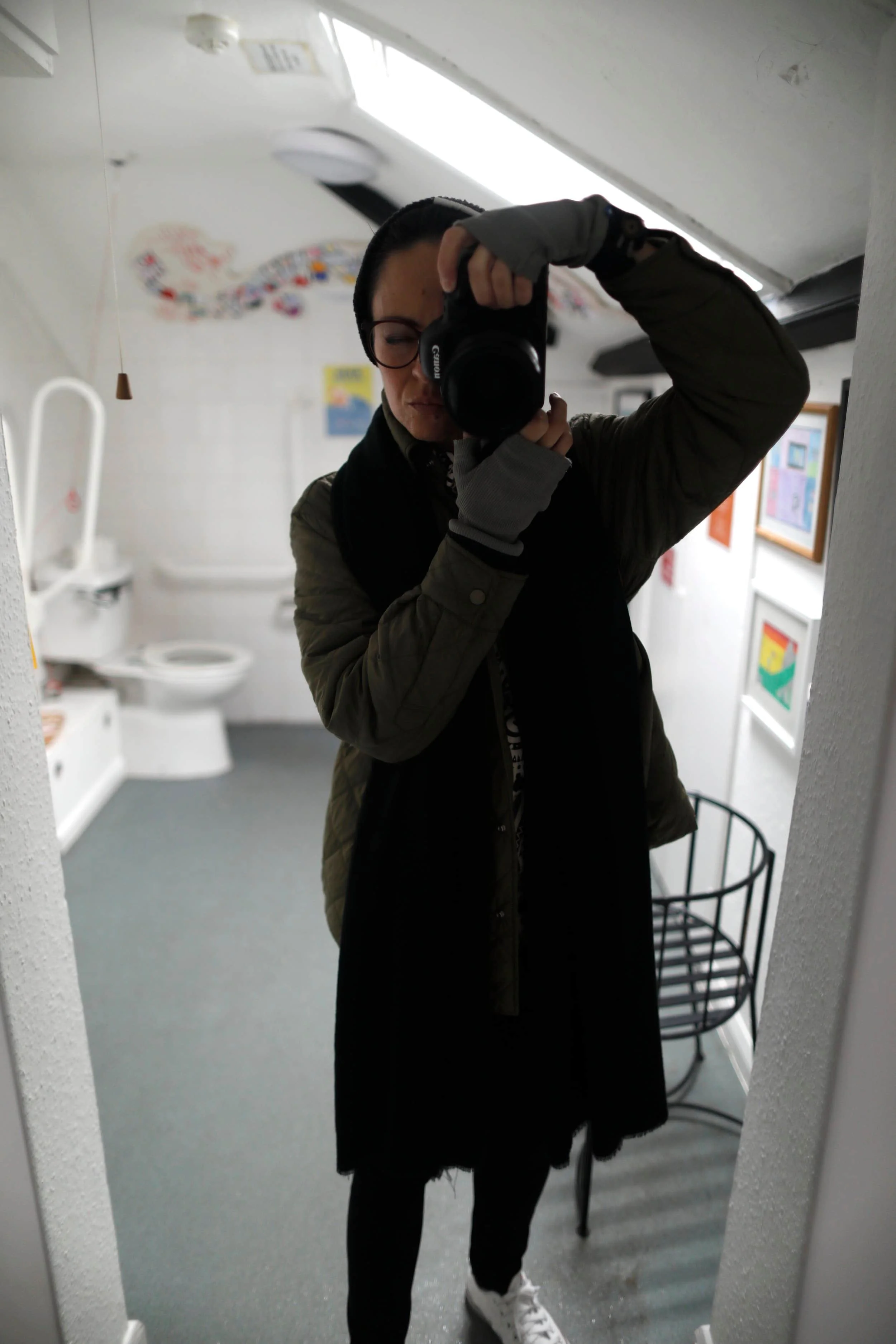 A girl wearing black taking photo of herself in a white bathroom