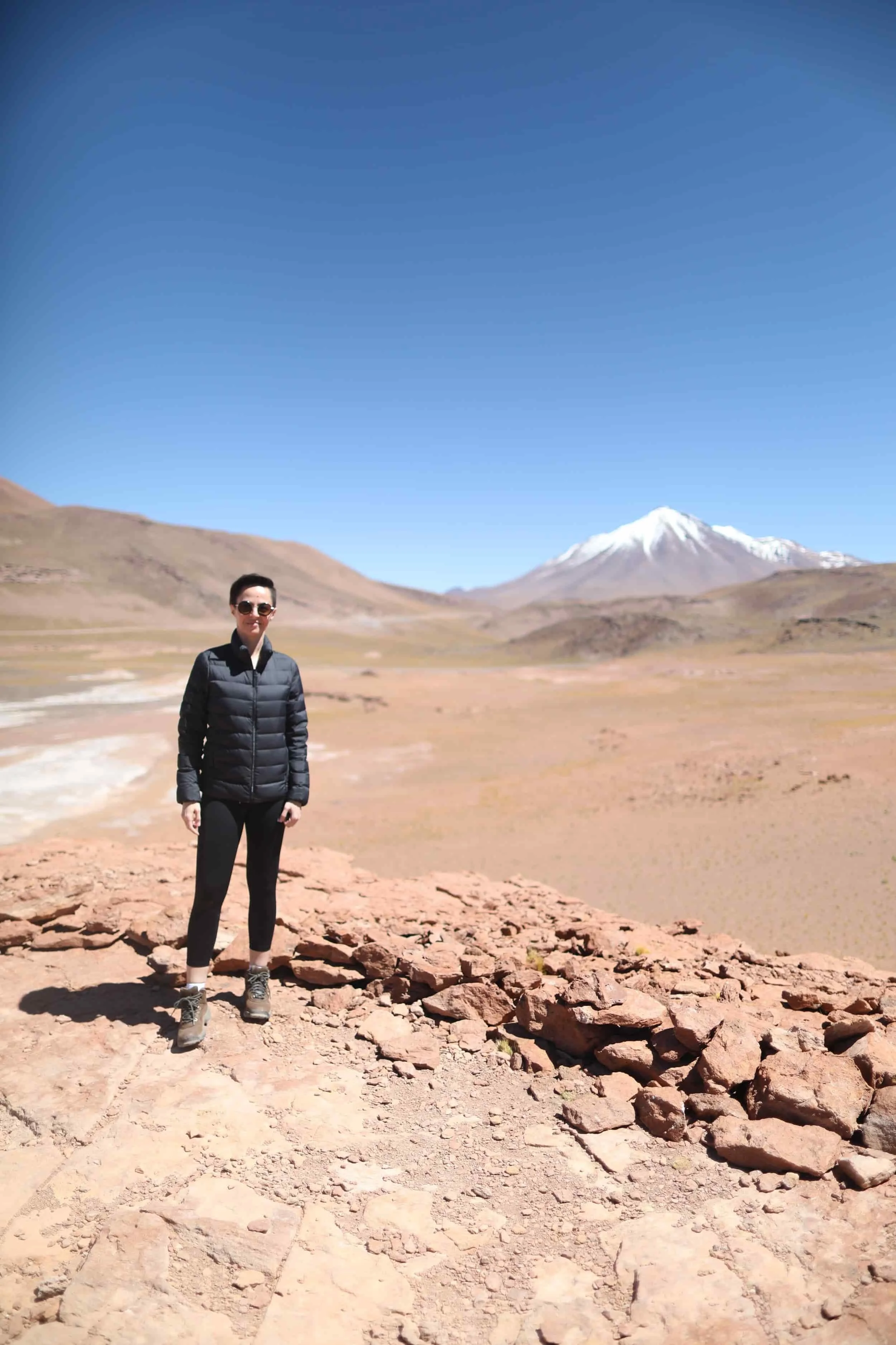 Girl standing in the desert with red rocks and mountains in the distance at Piedras Rojas in Atacama Desert in Chile