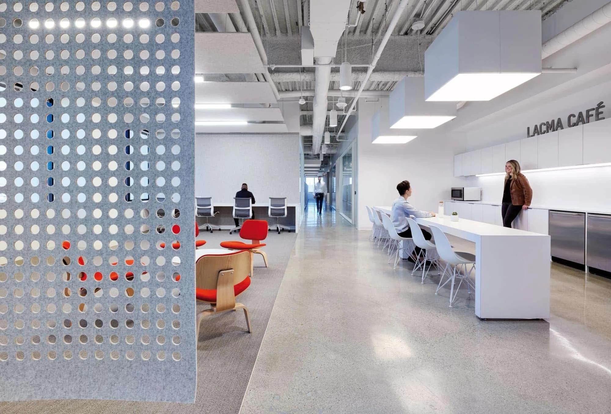 Interior view of office building with concrete flooring, grey carpet, orange seating and pantry.