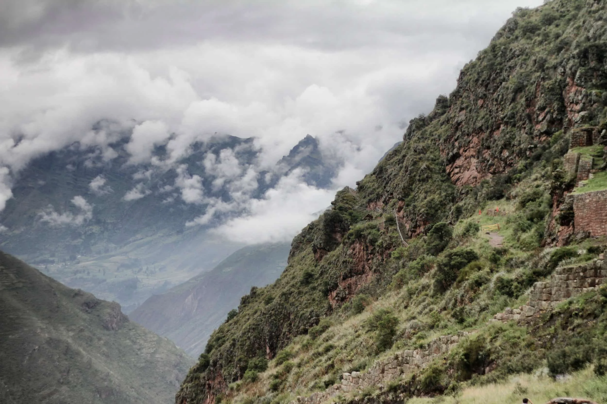View of mountainside in Sacred Valley, Peru with ruins built into mountain, clouds beyond