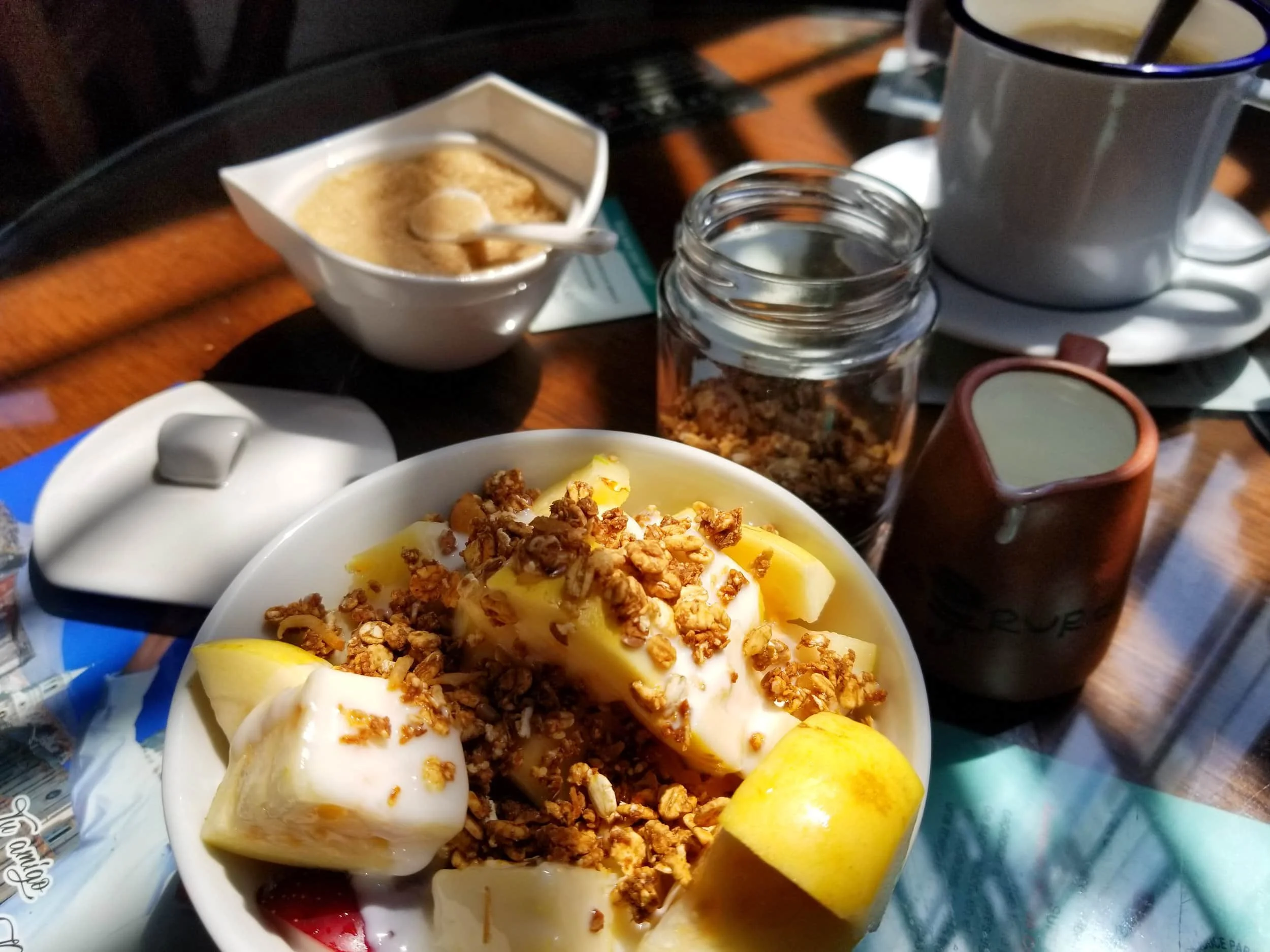 Table spread covered in shadow with breakfast of granola, yogurt and fruit