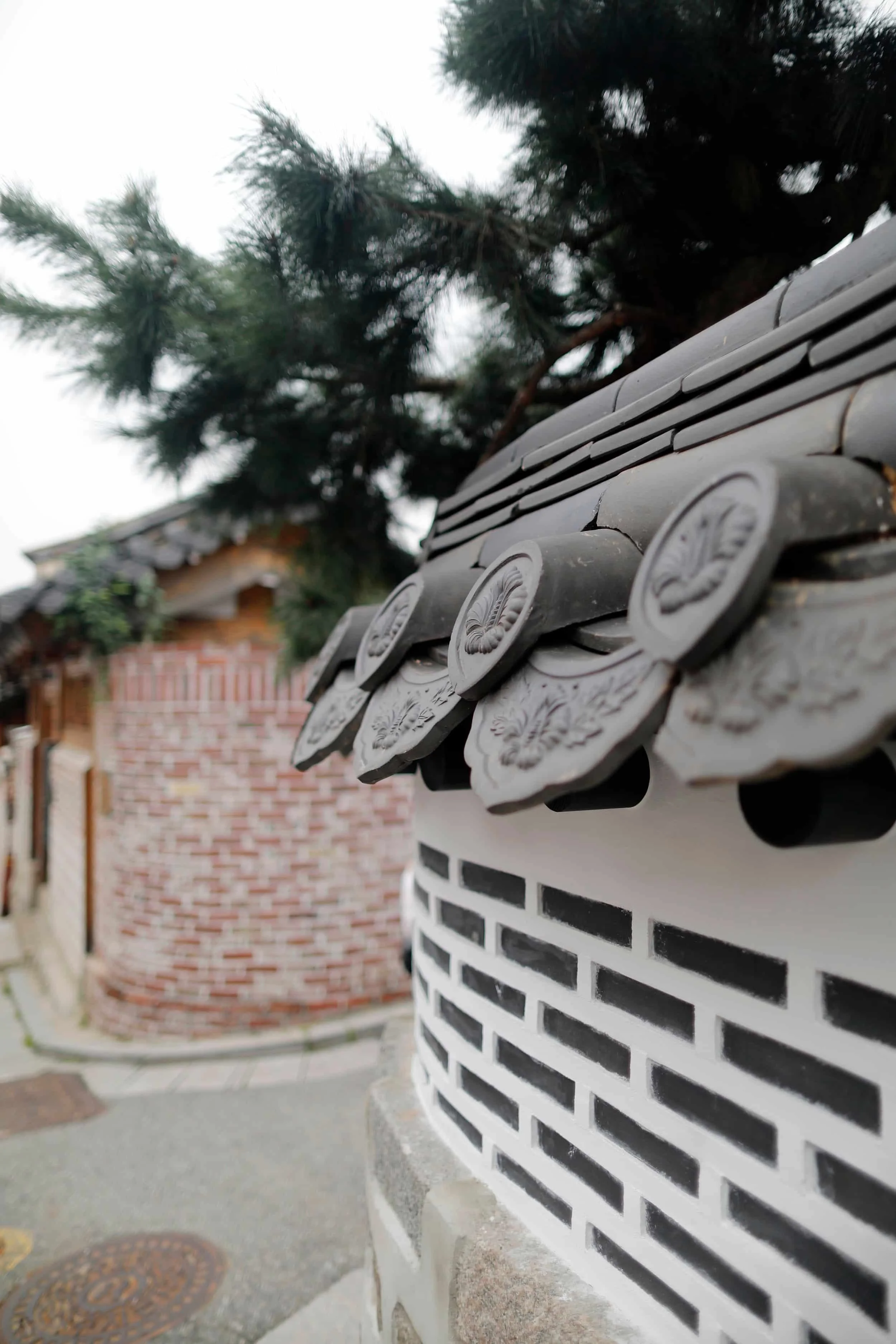 Close-up of a brick and white decorative wall with a traditional roof tile on the edge, and green trees in the background. Seoul, South Korea.