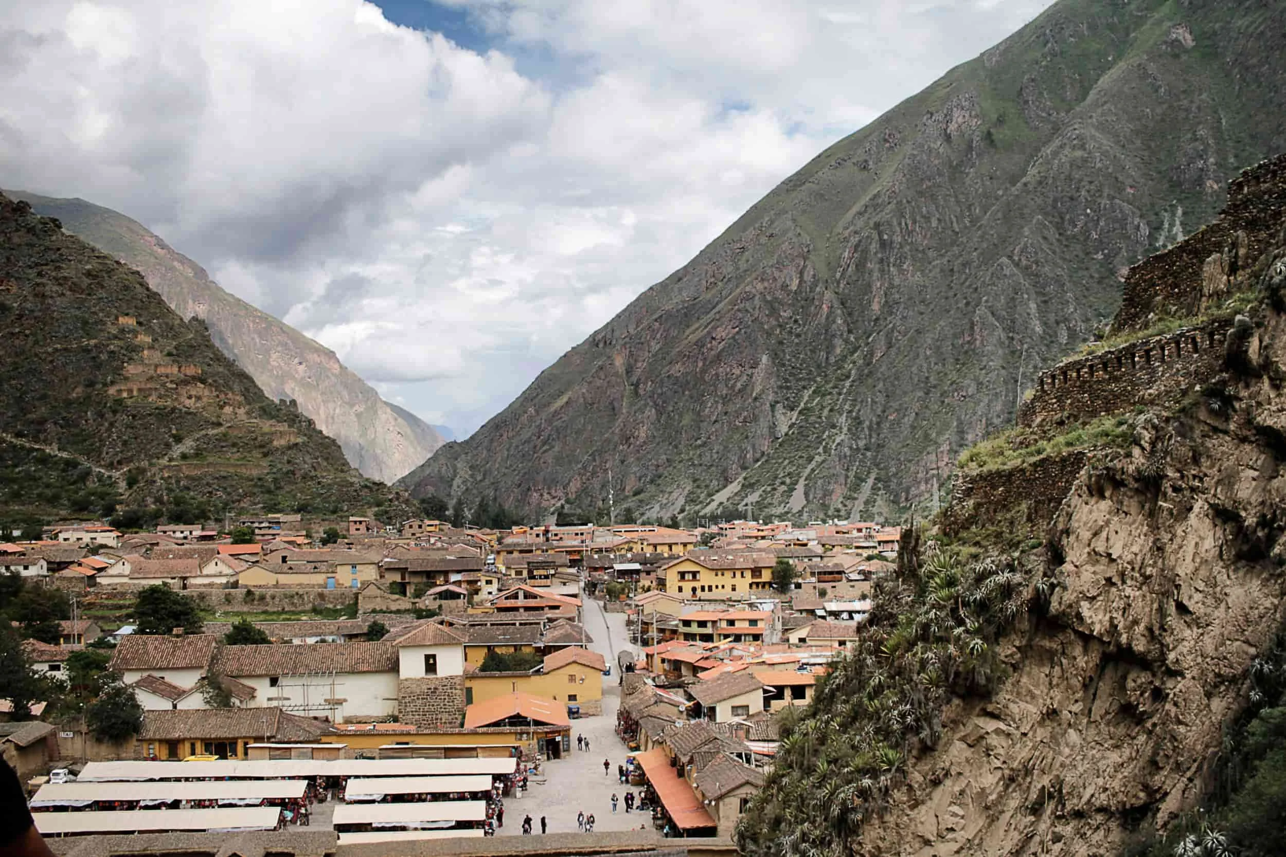 Village of Ollantaytambo in peru with colorful home tucked between massive mountains, clouds beyond