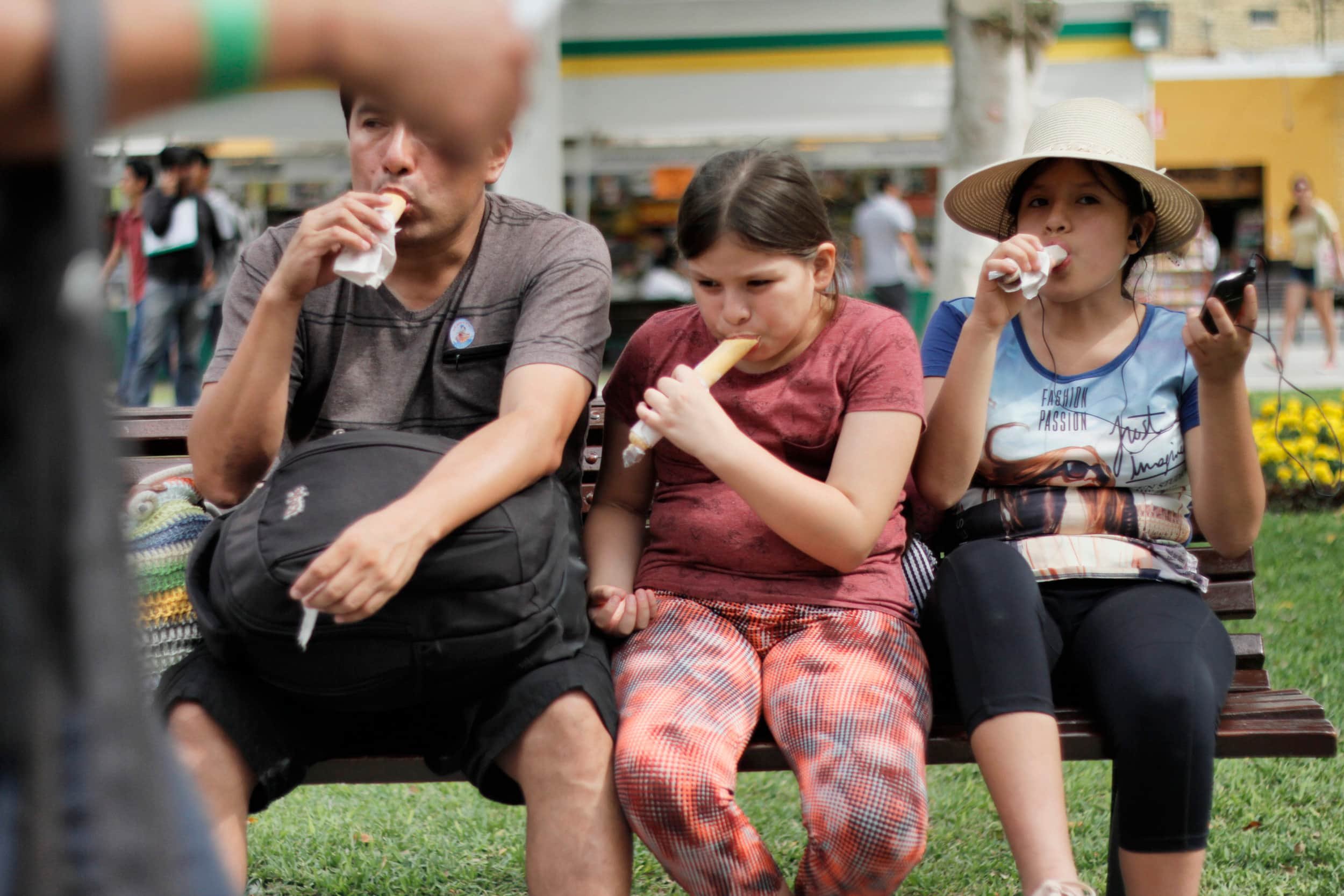 Family of father and two daughters sitting on a bench in Ica eating popsicles