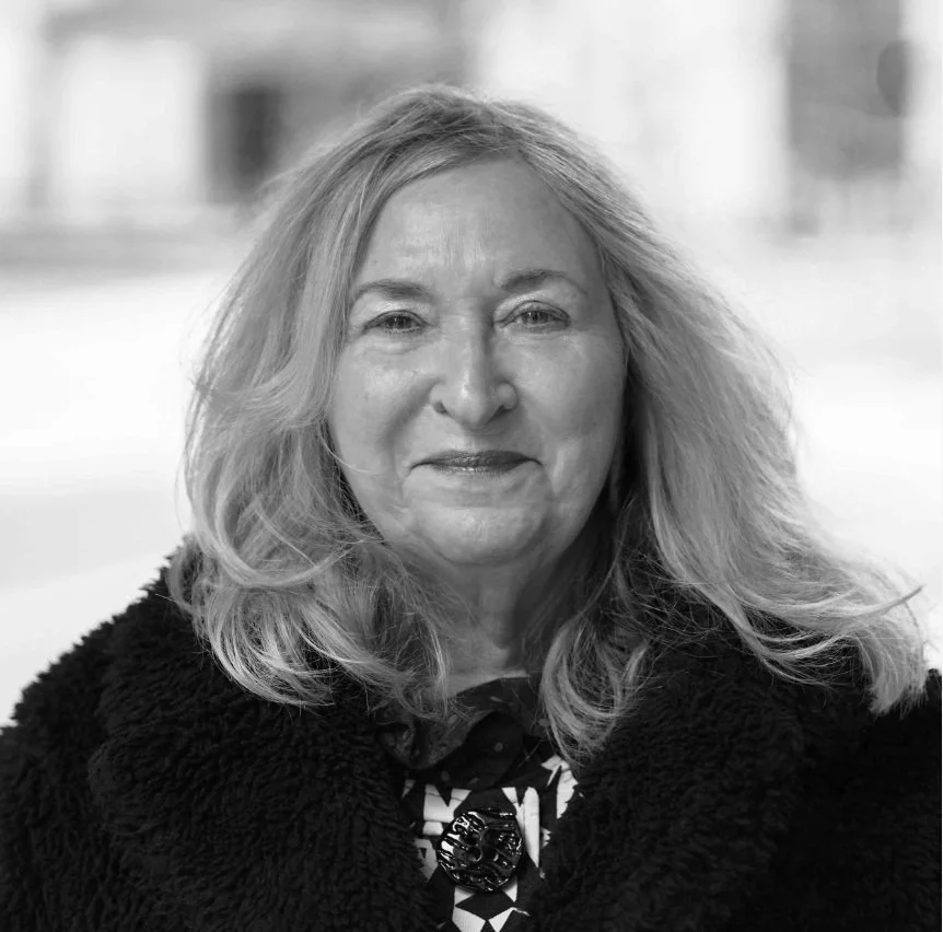 A black and white portrait of a woman with long, wavy hair wearing a dark, textured coat.