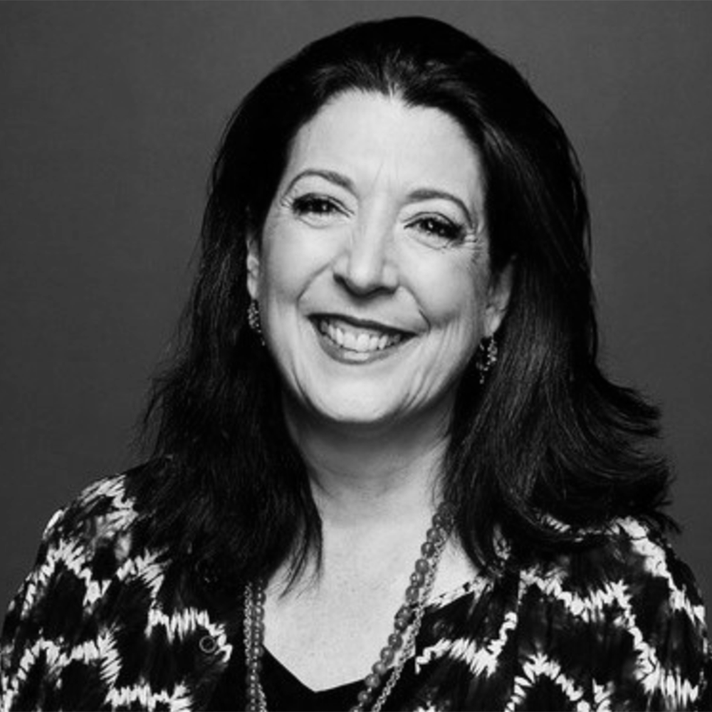 Black and white portrait of a smiling woman with dark hair, wearing earrings, a necklace, and a patterned top.