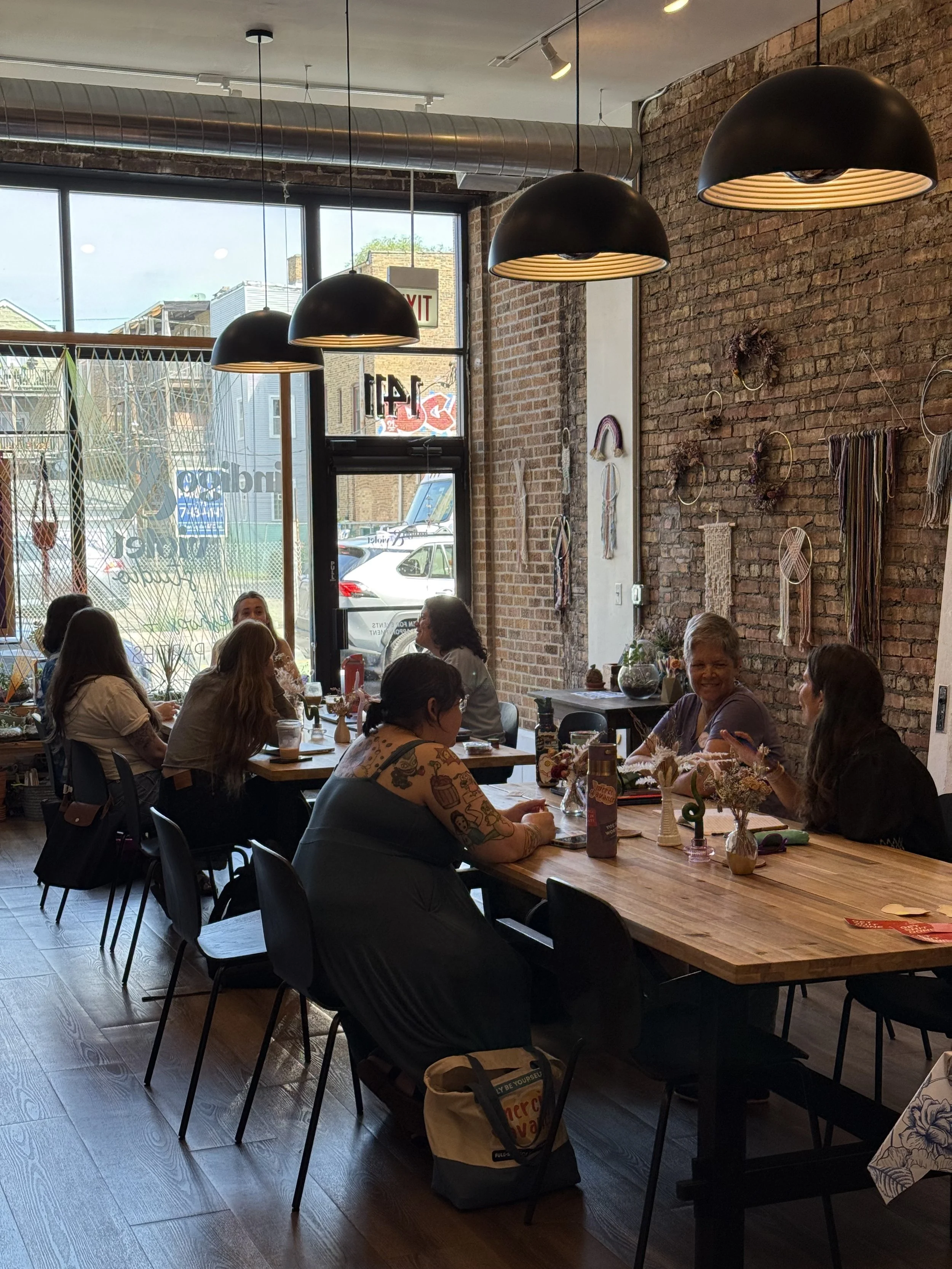 A group of female small business owners gather at two tables inside of Indigo and Violet craft studio to discuss business challenges and support each other.