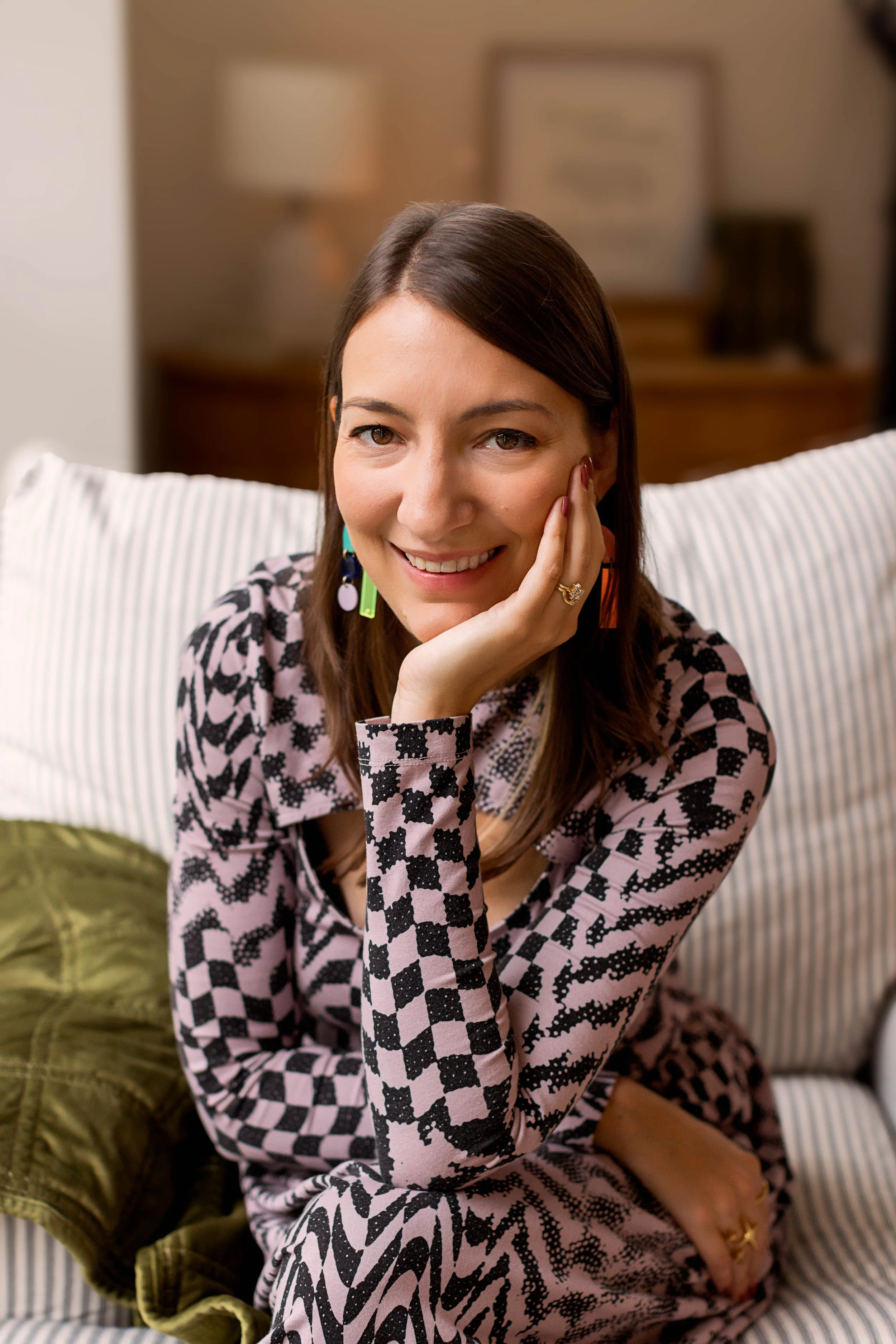 Chicago Souvenir Designer and Lettering Artist Smiles with her chin resting on her hand. She is wearing a light pink and black checkered dress.