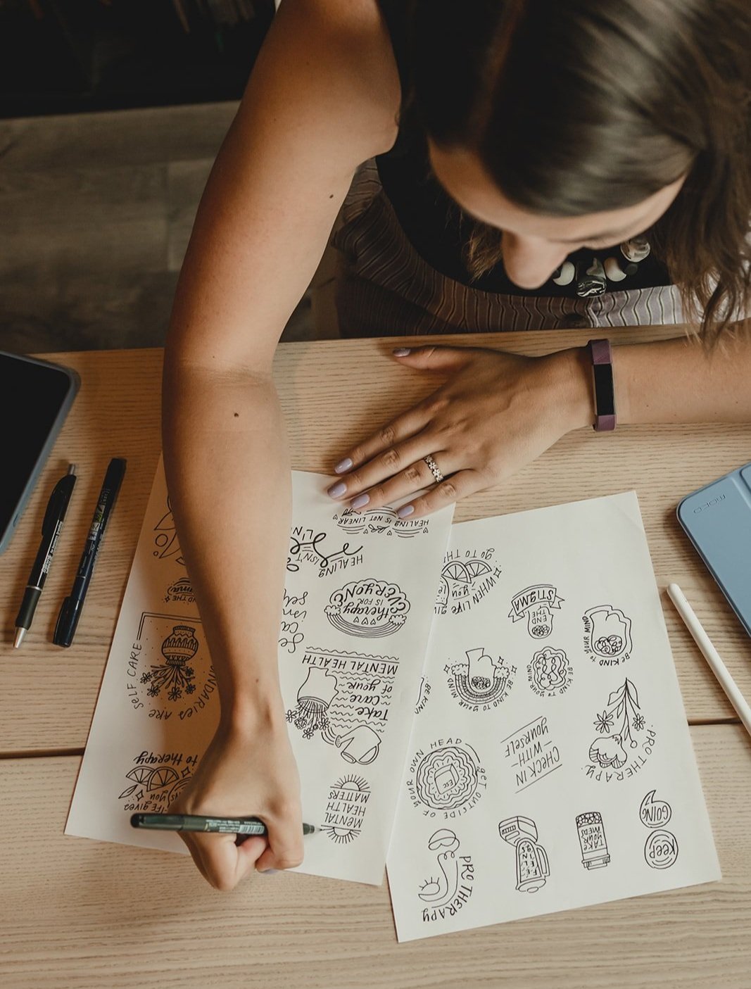 Top view of lettering artist Chelsie Tamms working on illustrating and hand-lettering a variety of stickers for mental health awareness