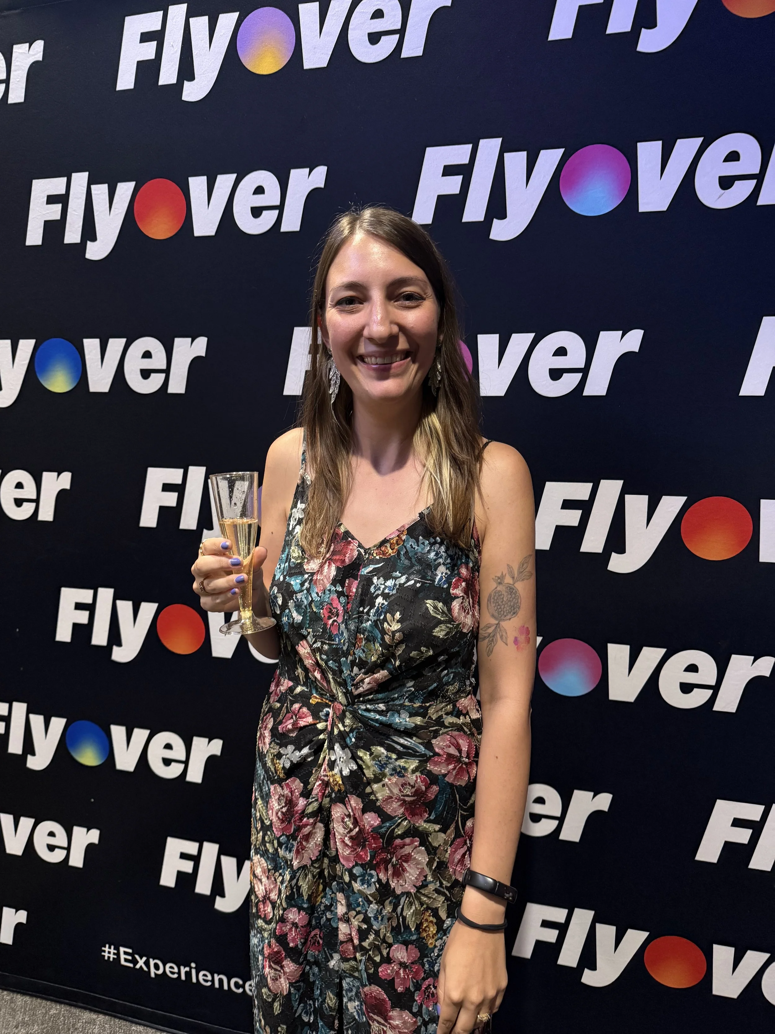 Artist Chelsie Tamms holds champagne in front of a Flyover banner backdrop at the 1 Millionth Rider Celebration