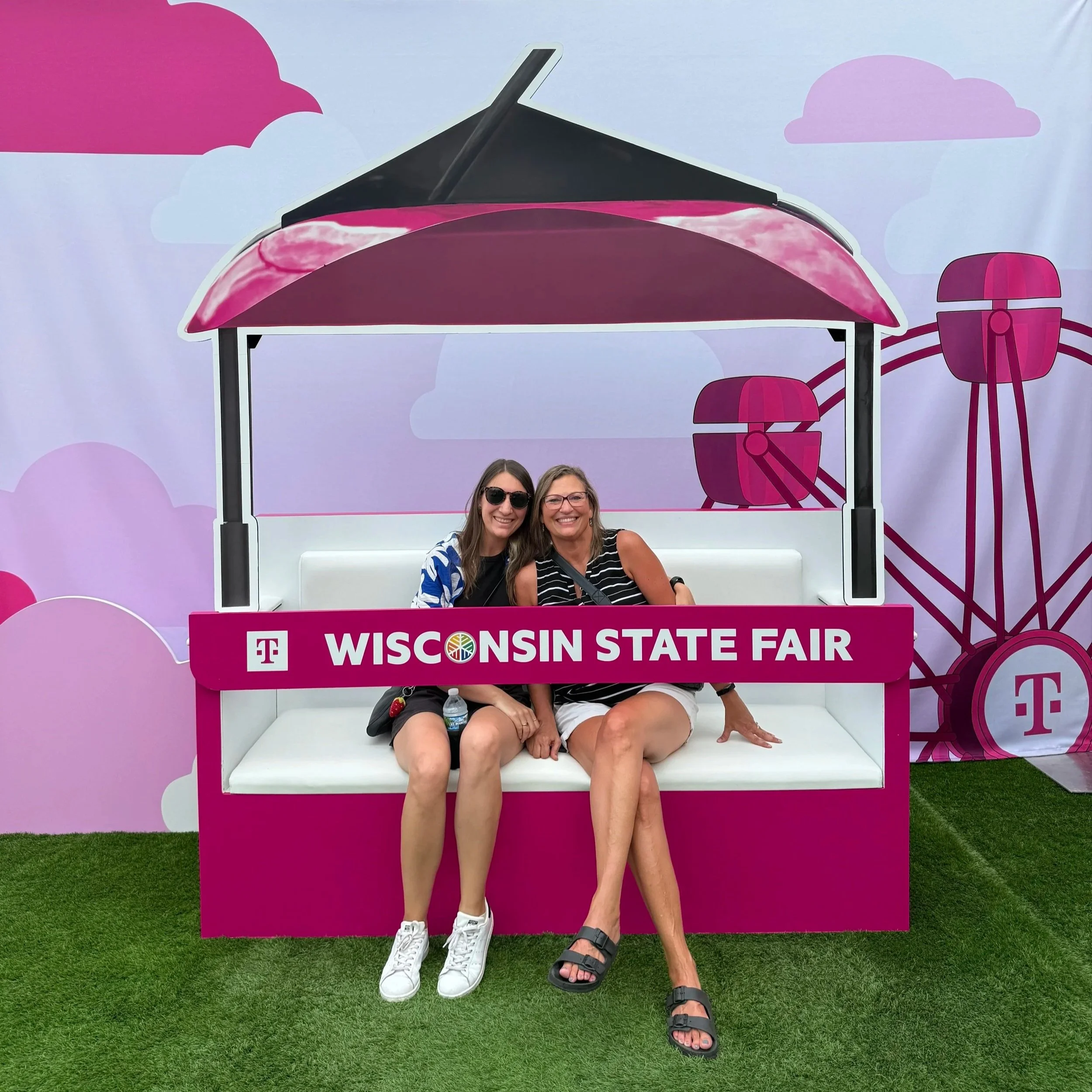 Chelsie and her mom sit inside a model Sky Glider seat in T-Mobile pink with a sign that reads Wisconsin State Fair