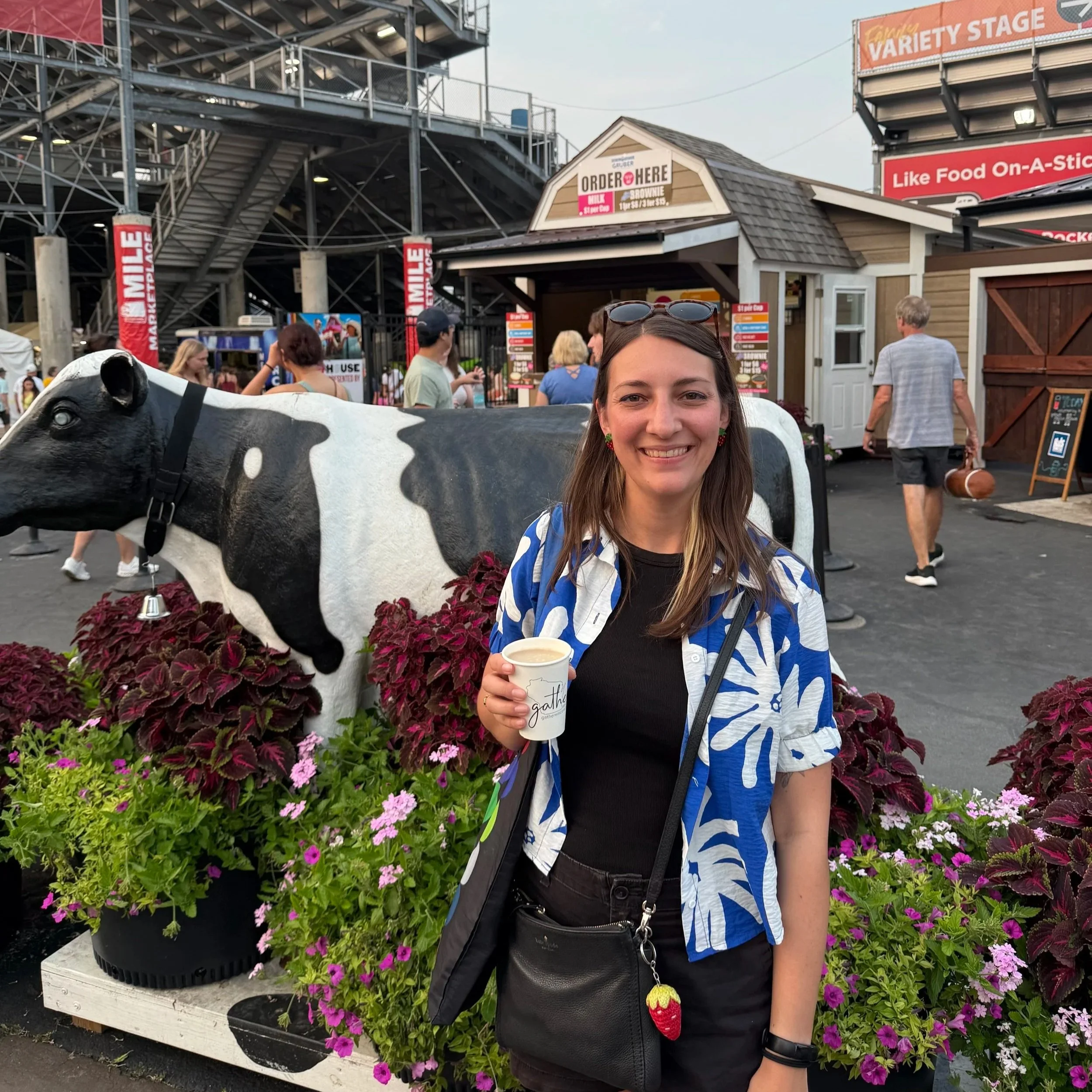 Chelsie stands in front of a cow statue by the Milk House at Wisconsin State Fair. She is holding a glass of root beer flavored milk and smiling.