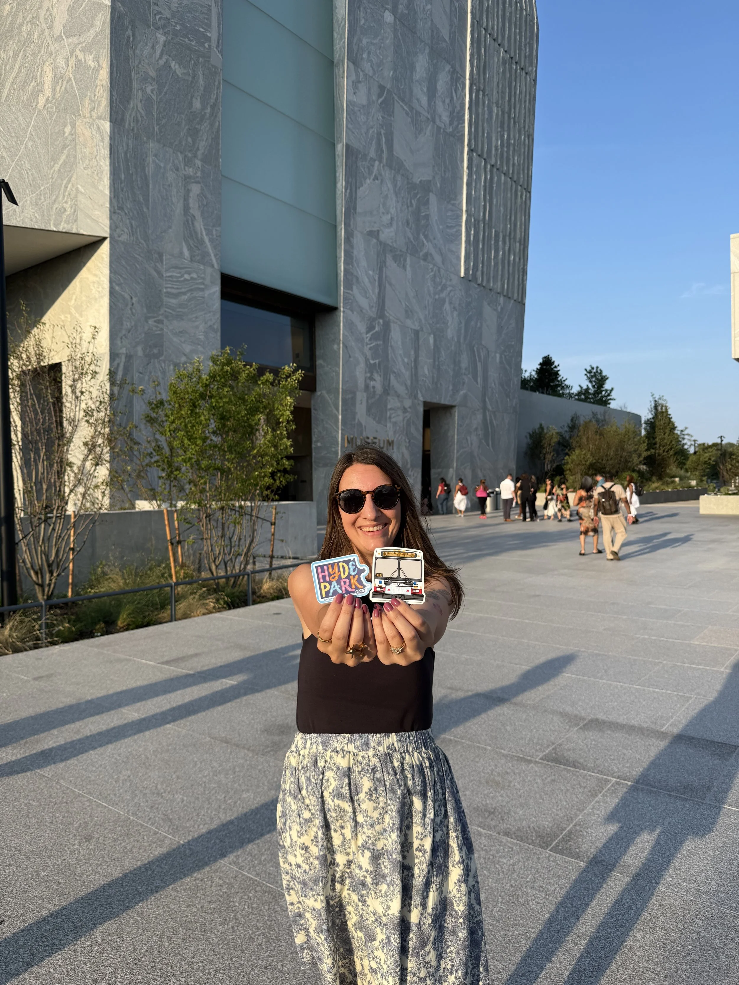 Chicago Artist Chelsie Tamms holds new Chicago Souvenir Stickers for the Obama Presidential Center in front of the Museum