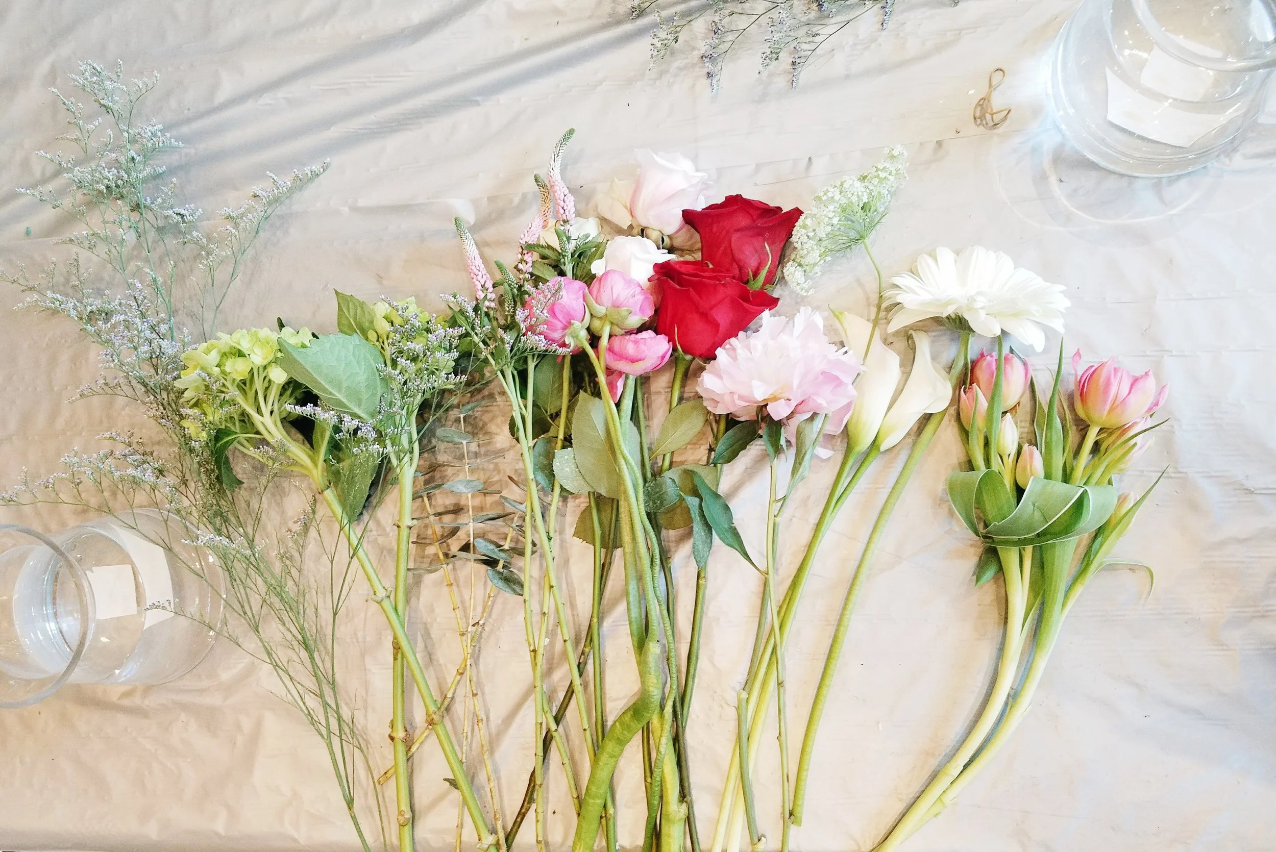 Left to Right: Limonium, hydrangeas, celosia, ranunculus, white roses, red roses, peony, calla lilies, bouvardia, gerber daisy, and tulips. 