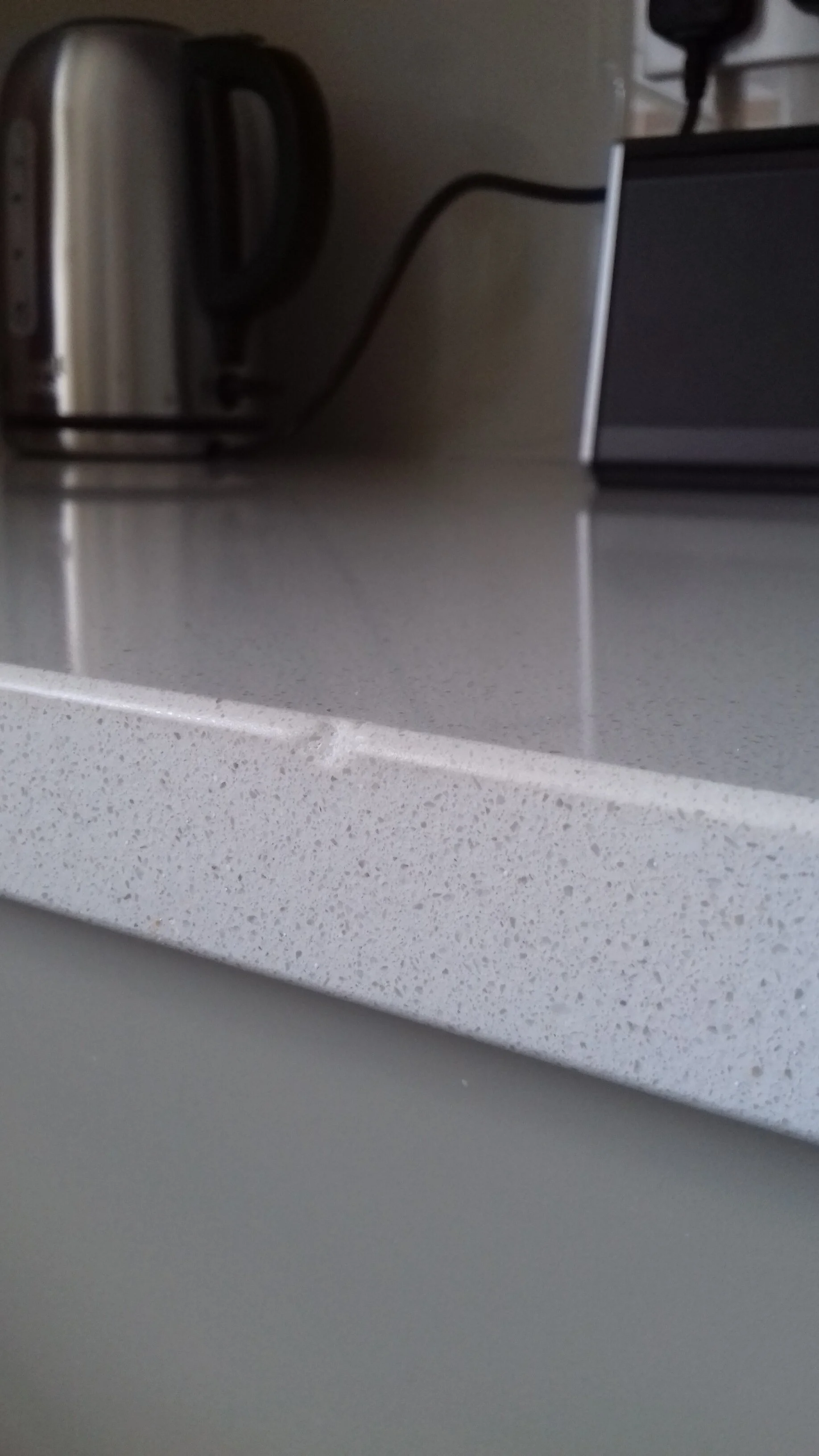 Close-up of a chipped quartz kitchen worktop with a black toaster, silver kettle, and black coffee machine.