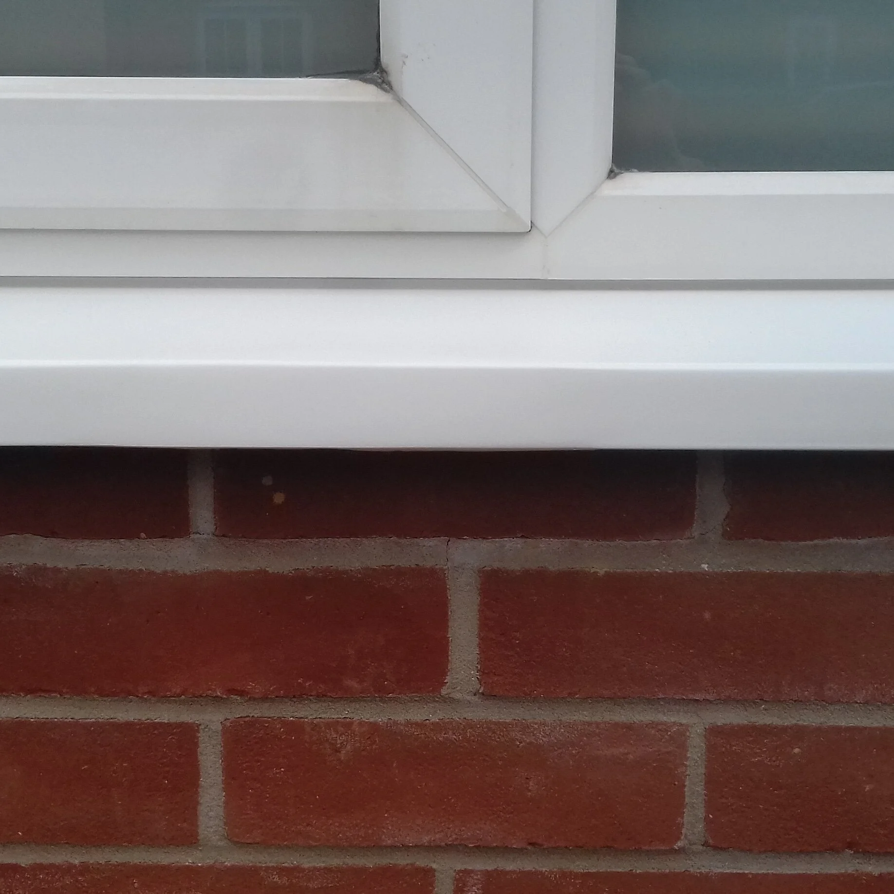 Close-up of a white window frame and sill above a brick wall.