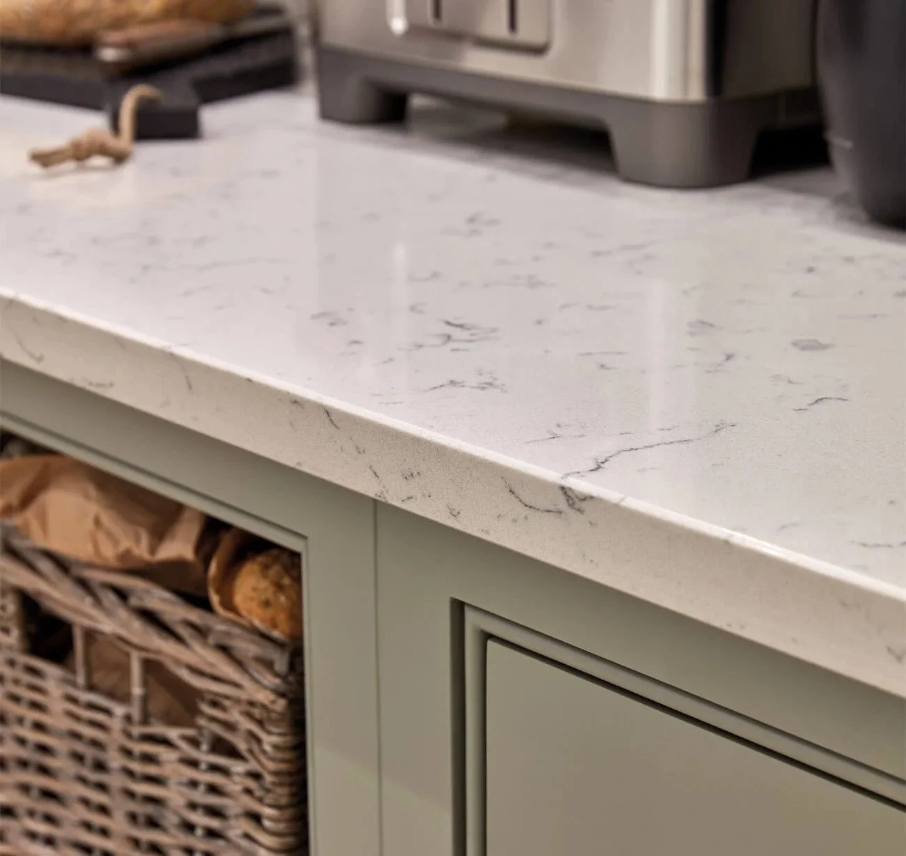 Close-up of a kitchen worktop made of white marble with gray veining, adjacent to beige cabinets