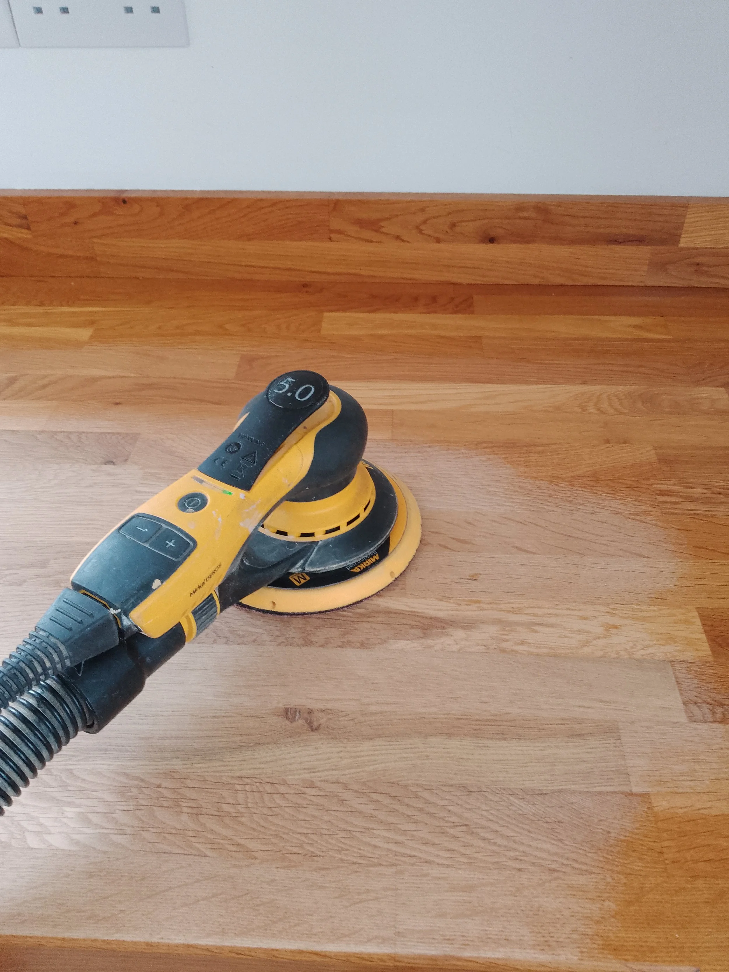 A yellow and black handheld sander on a wood worktop
