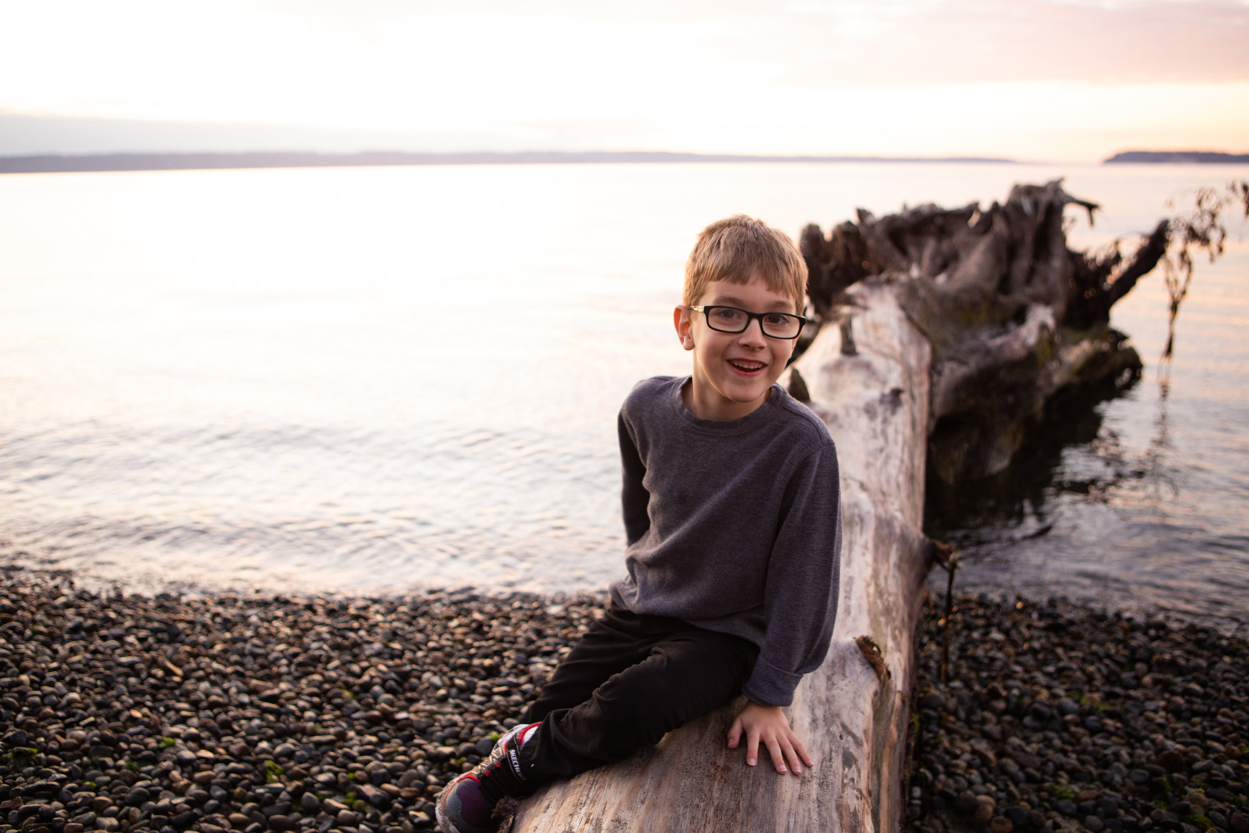 Boy smiling while sitting on log on a pebbly beach