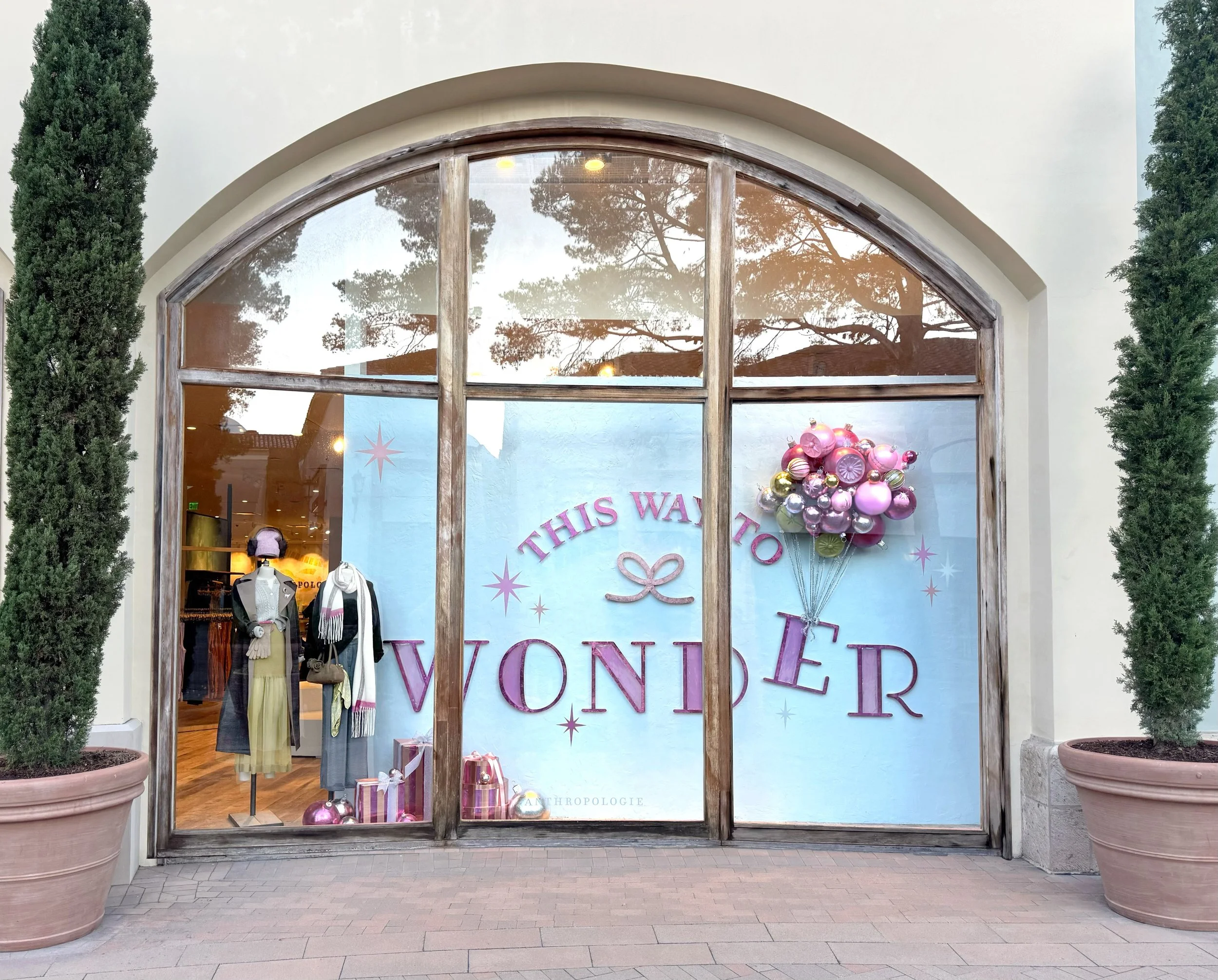    Anthropologie Holiday ‘25 Window:    Ornaments sculpted from foam and plaster. On glass painted sparkles. Sign laser cut and pink foiled.   