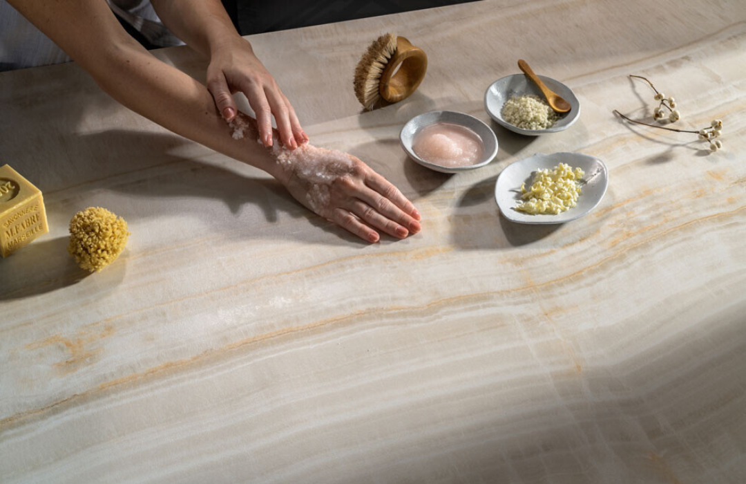 Hands applying bath salts on a light veined Porcelain countertop with spa items