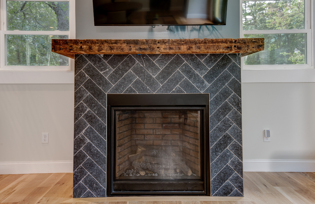 Close-up of a herringbone-pattern tile fireplace surround with a reclaimed wood mantel