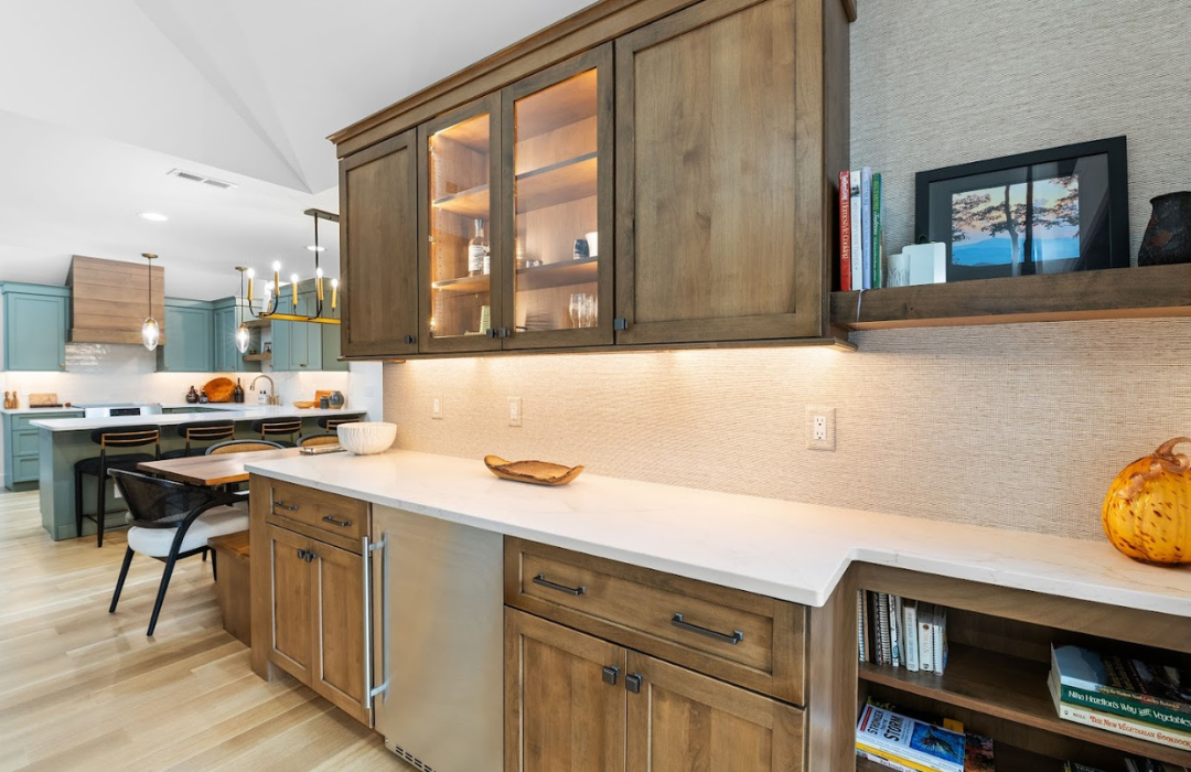 Modern kitchen with natural wood cabinets featuring glass-front upper cabinets, white quartz countertops, and sage green island in Asheville home