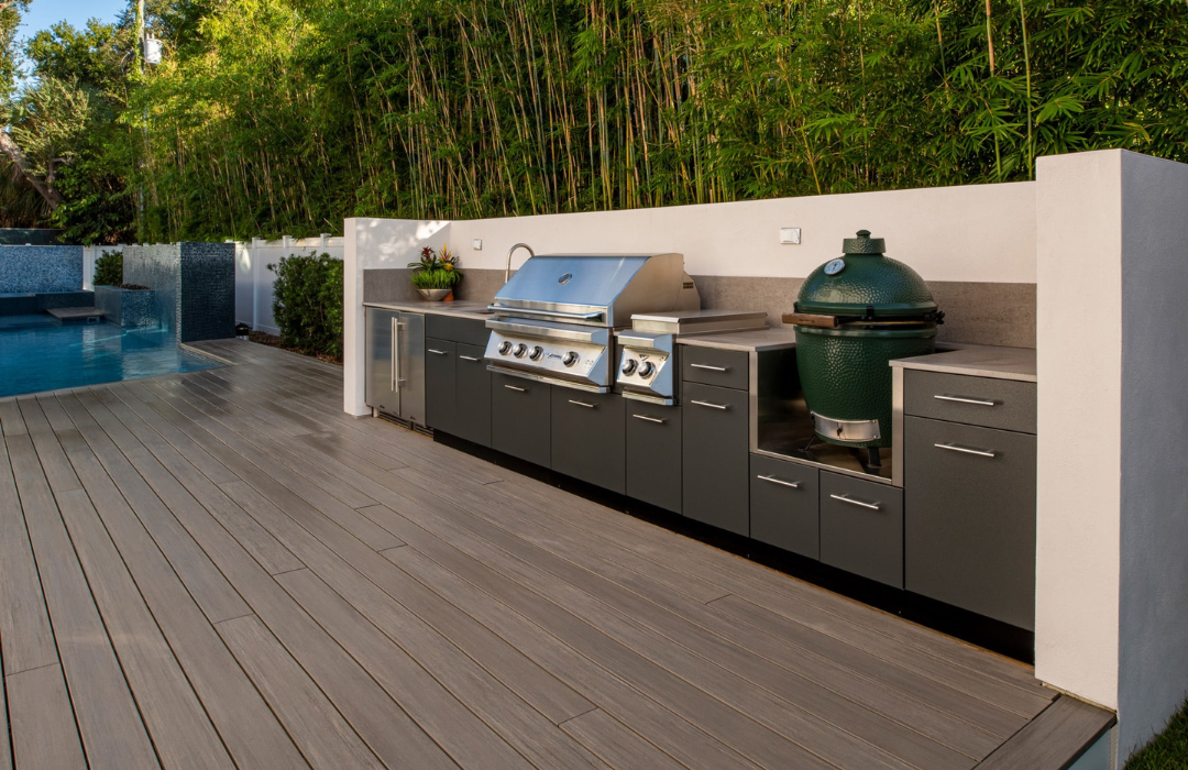 Sleek outdoor kitchen with dark stainless steel cabinets, gray sintered stone countertop, built-in grill, and Big Green Egg on a composite deck