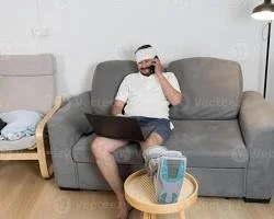 Self-employed practitioner working on a laptop while recovering on bed rest due to an orthopedic injury, managing clinic administration remotely.
