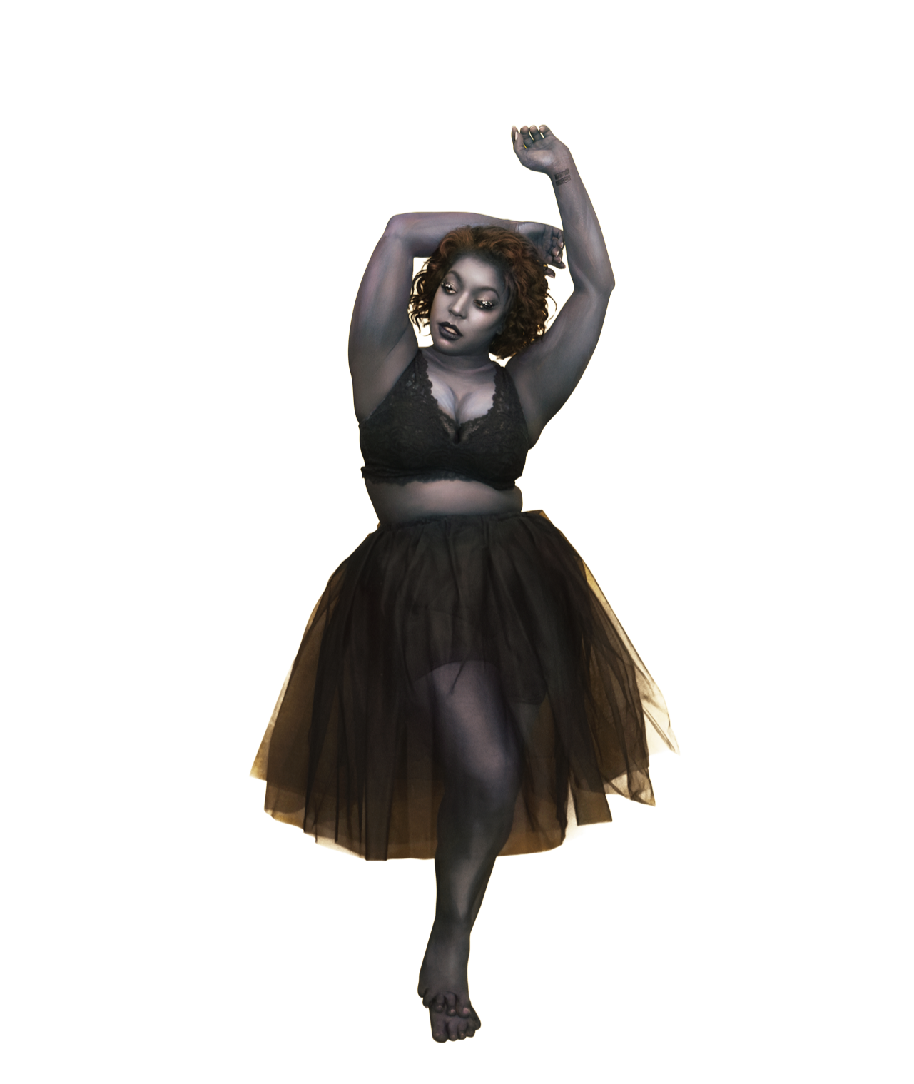 A woman with curly hair posing with arms raised above her head, wearing a black lace bralette and a black tulle skirt